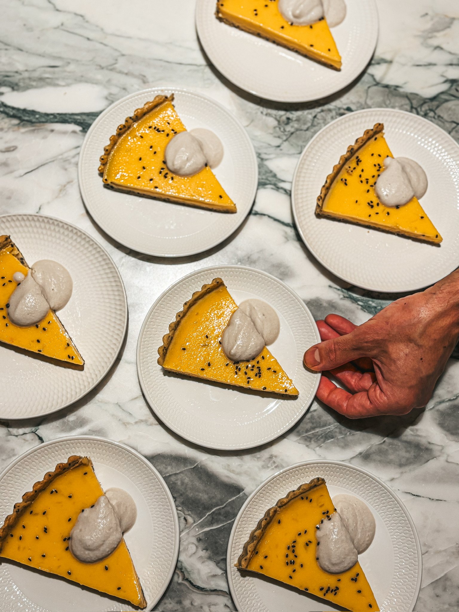 Slices of lemon tart with whipped cream on small white plates on a marble surface.