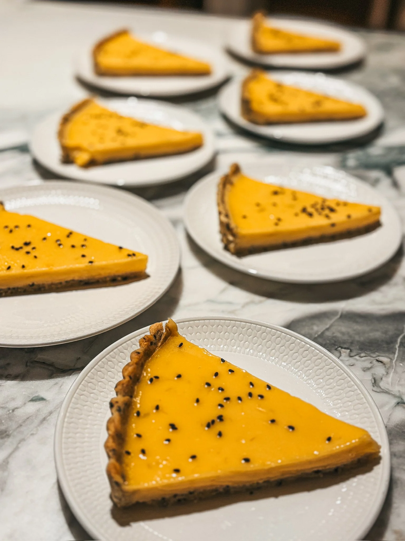 Multiple slices of glossy orange cheesecake topped with black sesame seeds on white plates.