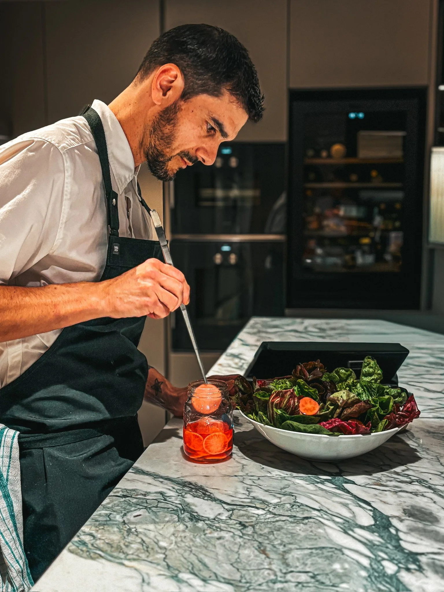 Chef in an apron preparing a colorful salad with dressing in a modern kitchen