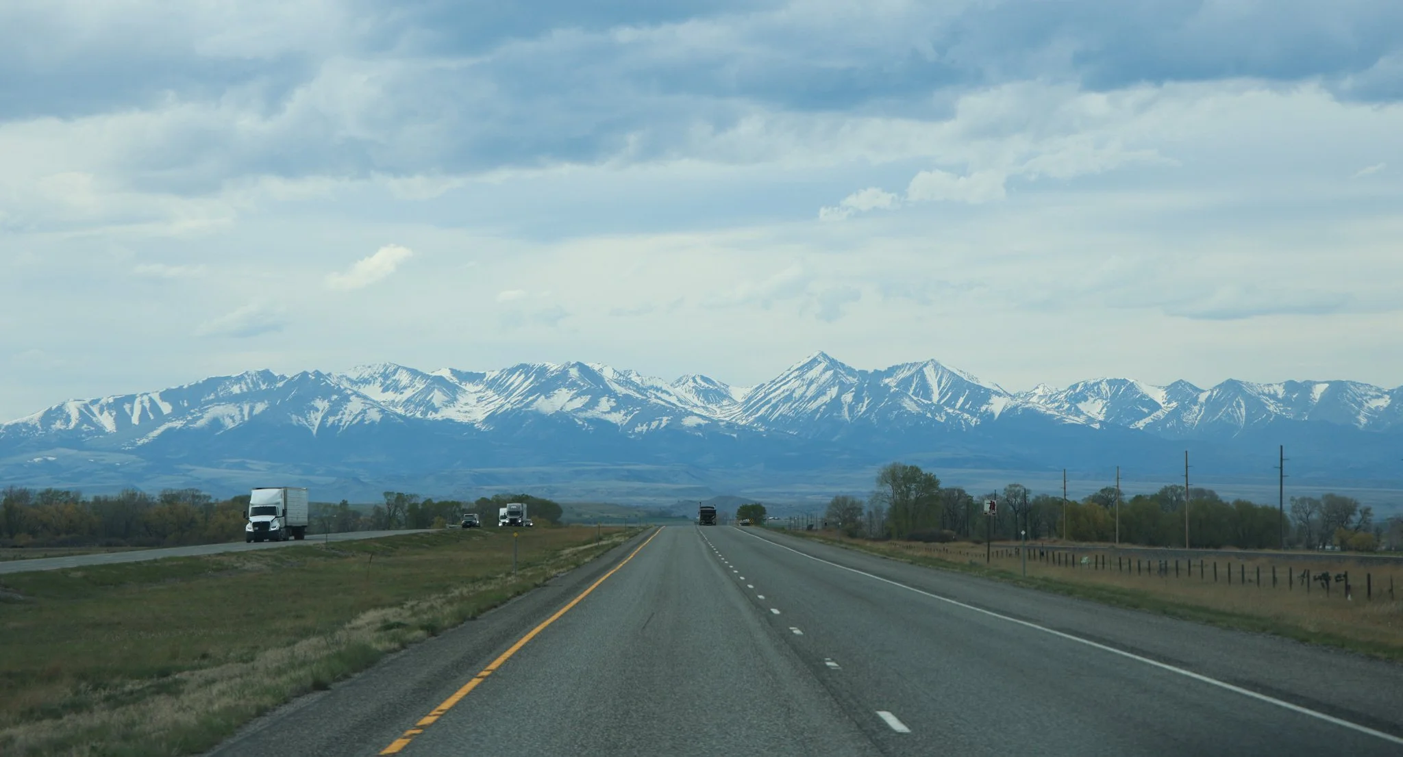 A highway leading towards snow-capped mountains in the distance under a cloudy sky.