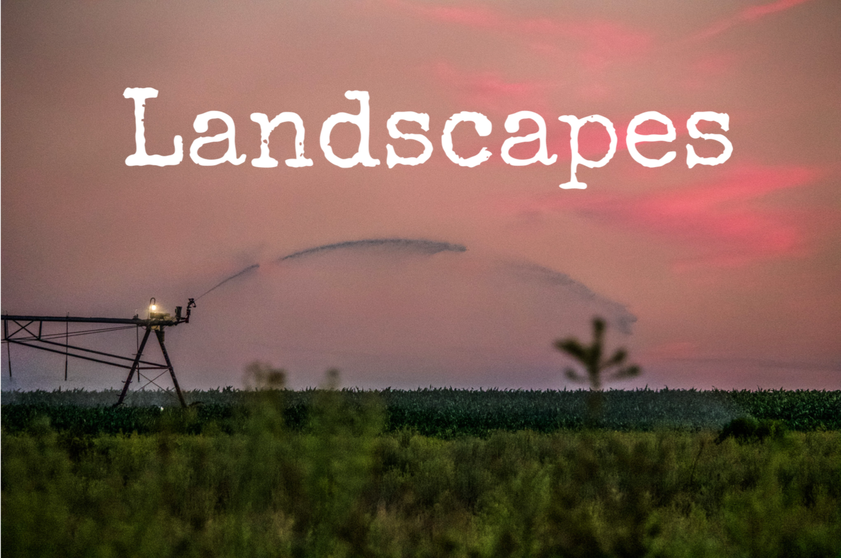 A rural landscape at sunset with a horizon filled with pink and purple clouds, a silhouette of a farm field, and an irrigation sprinkler spraying water across the field.