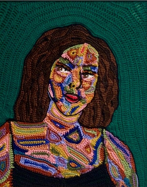 Colorful embroidered portrait of a woman with shoulder-length brown hair and red lipstick on a green background.