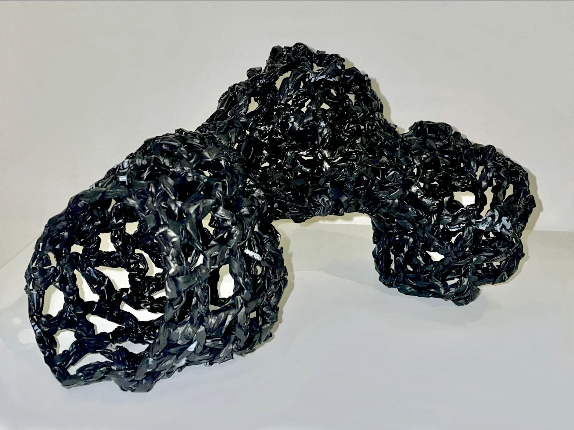 Black woven sculpture resembling a torus with an irregular, open lattice structure.