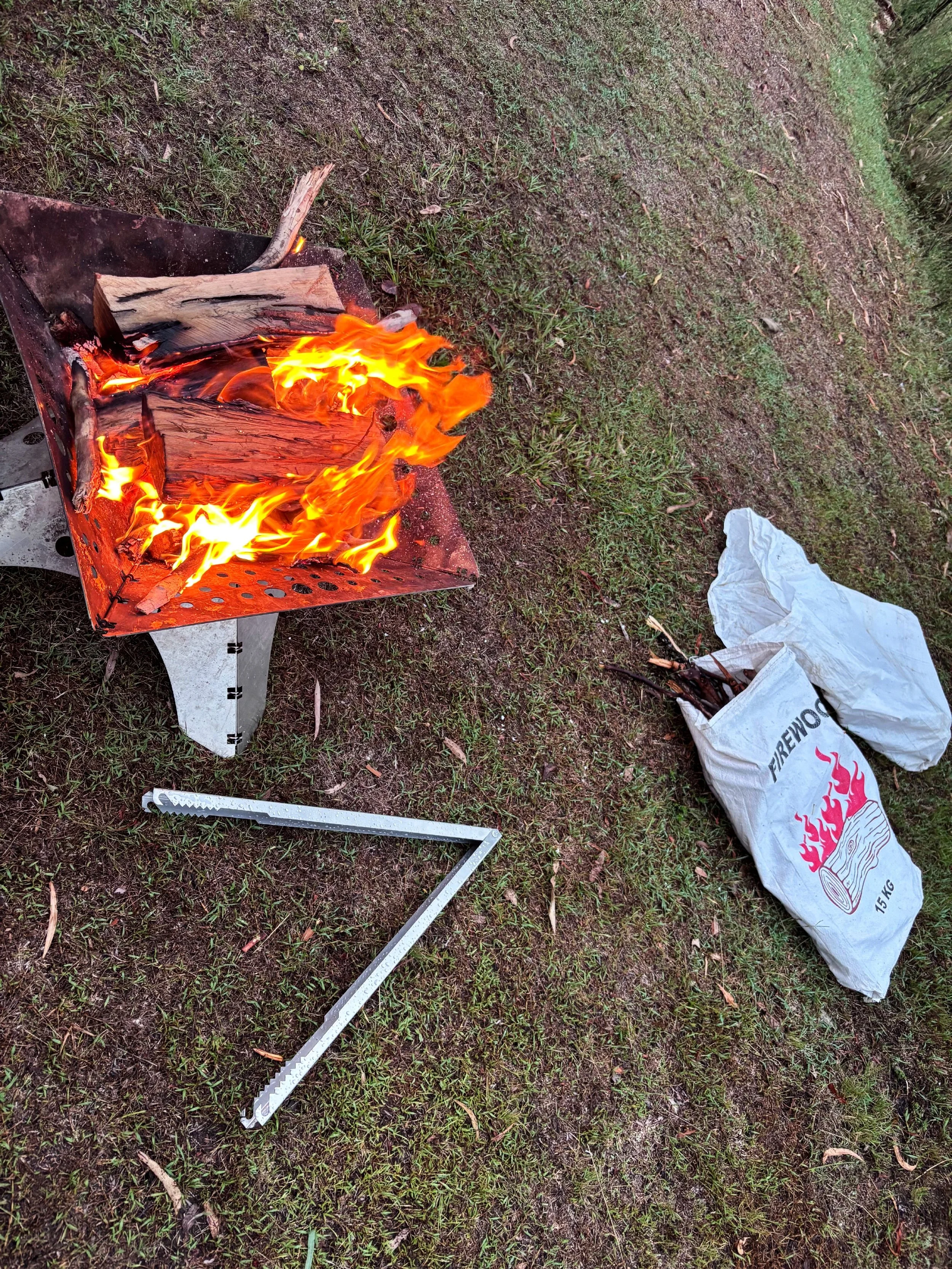 Two men outdoors with a set of Tongs for Tossers Campfire Tongs with a fire pit between them.