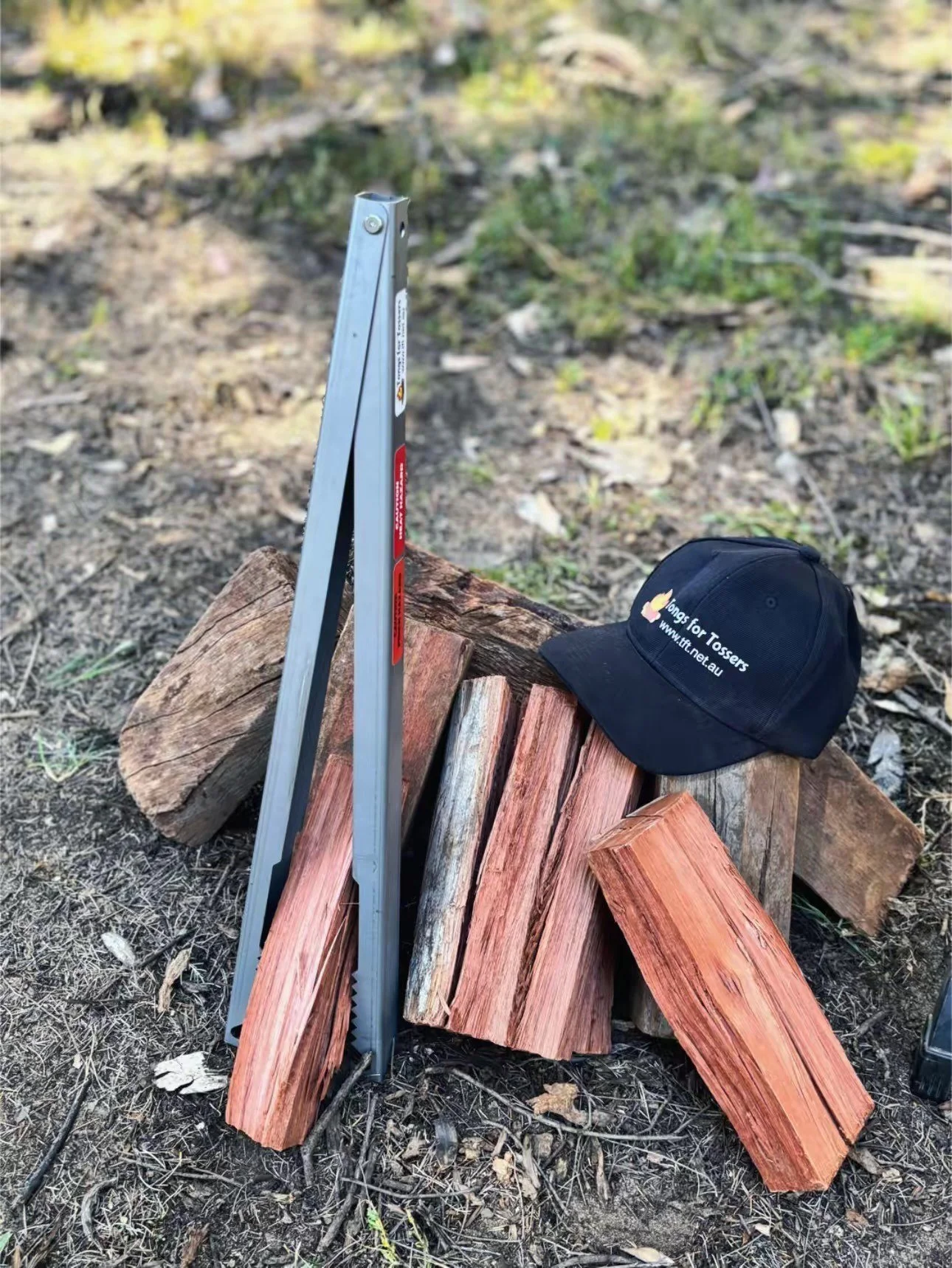 Tongs for Tossers near some firewood, with a Stubby Cooler and a Tongs for Tossers Hat