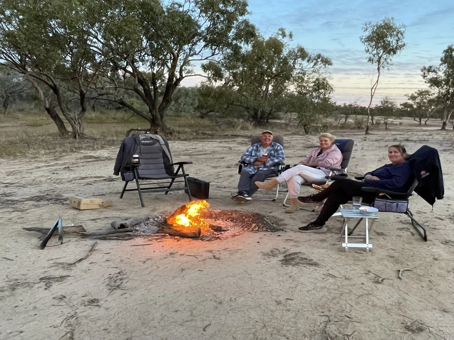 Friends camping with campfire and using Tongs for Tossers to move hot logs and burning wood