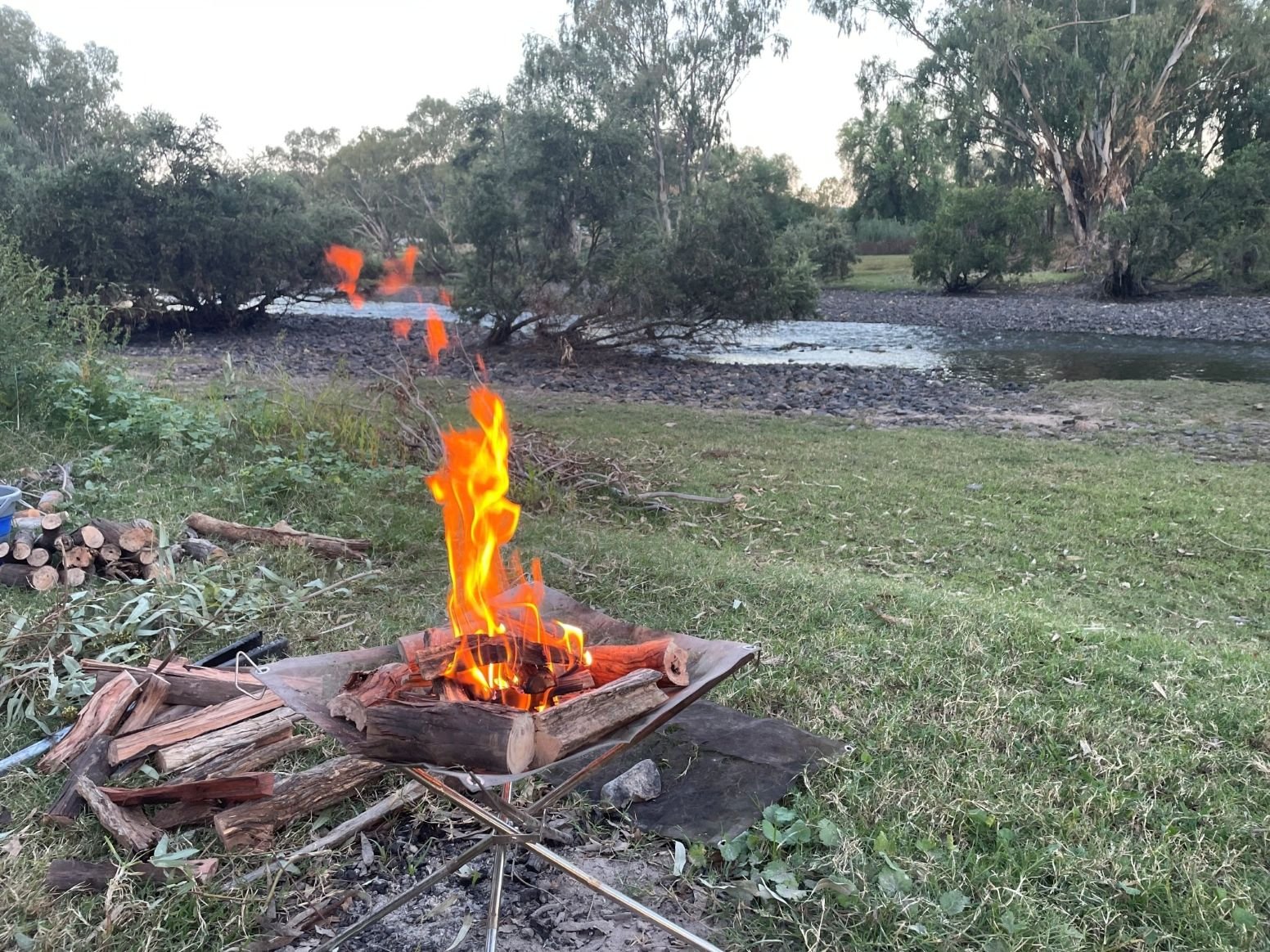 Tongs for Tossers with Campfire on Bank of River with Firewood