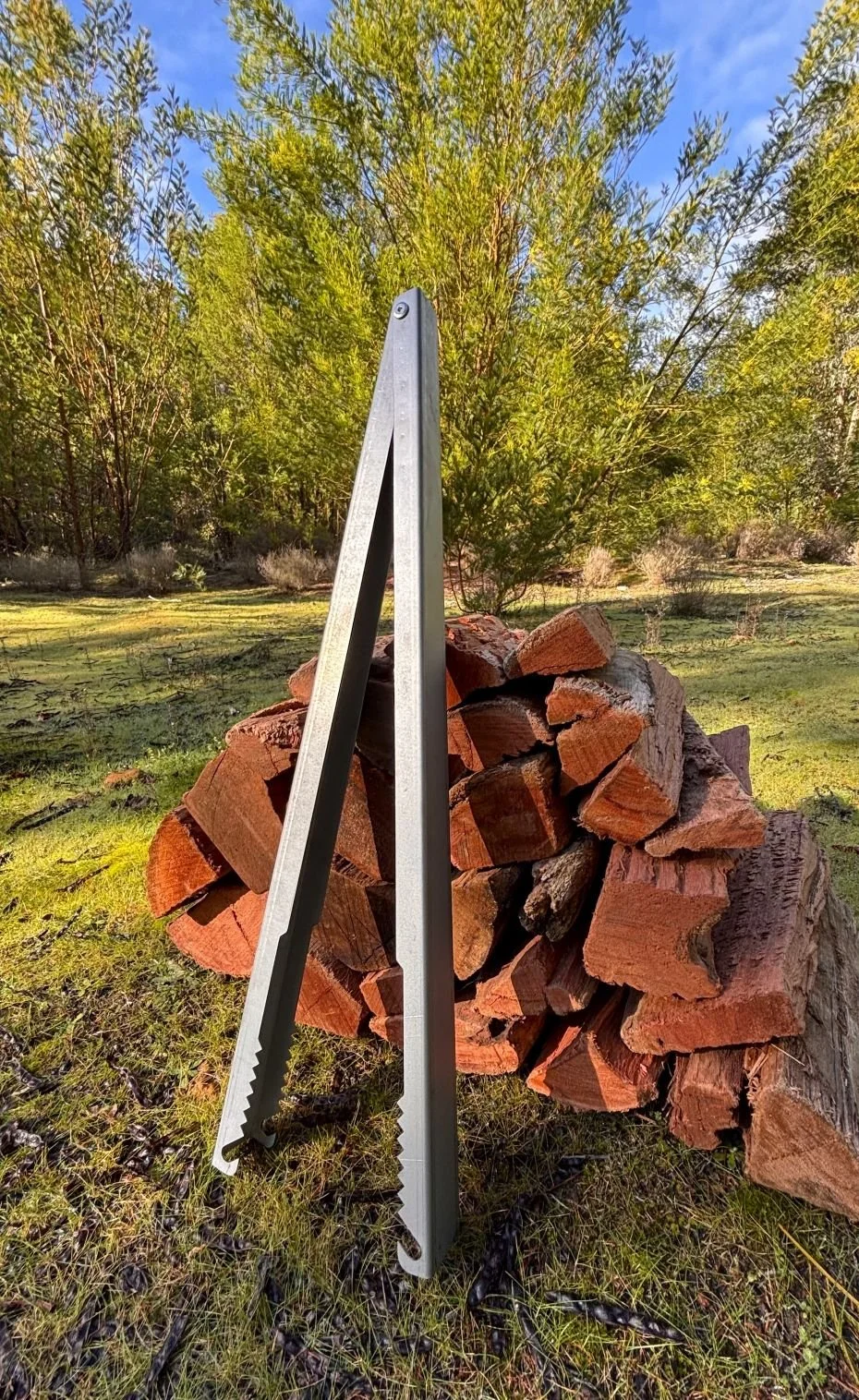 Campfire Tongs leaning against a pile of firewood, Tongs for Tossers