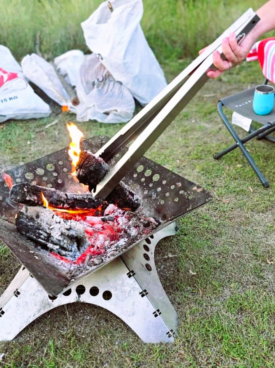 A person using Tongs for Tossers Fire Tongs to place a piece of wood in the fire pit for the safety of people.