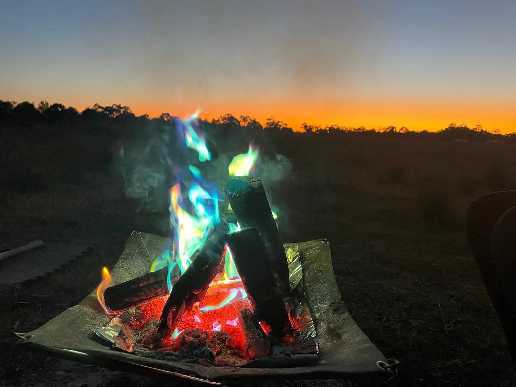 Multicolored campfire burning at a campsite during sunset with Tongs for Tossers to safely handle the burning wood