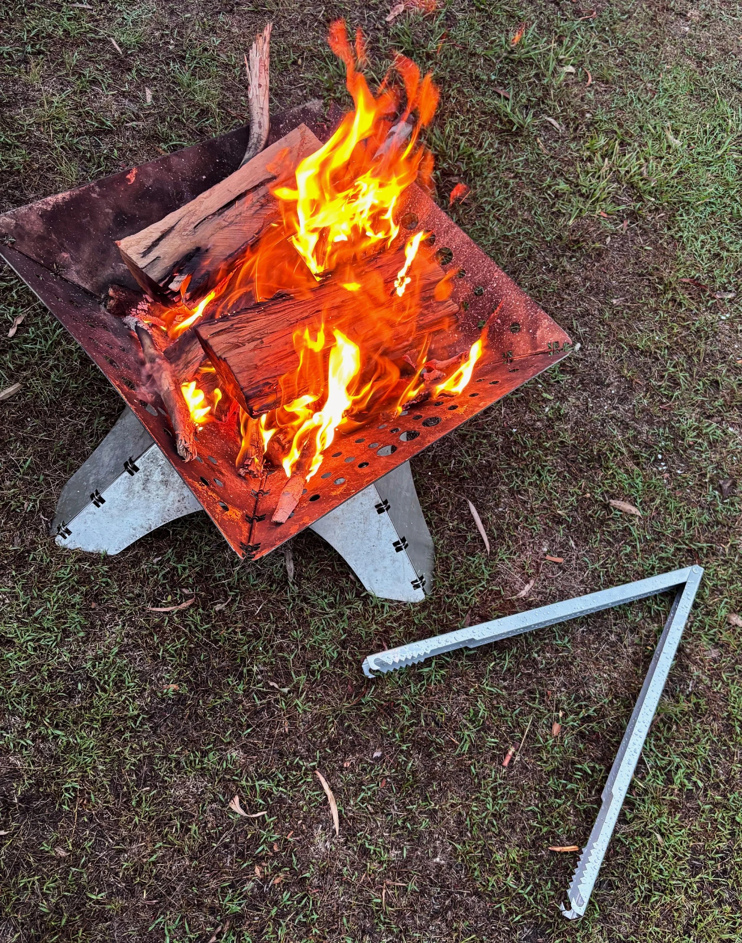 Tongs for Tossers with Campfire on Bank of River with Firewood
