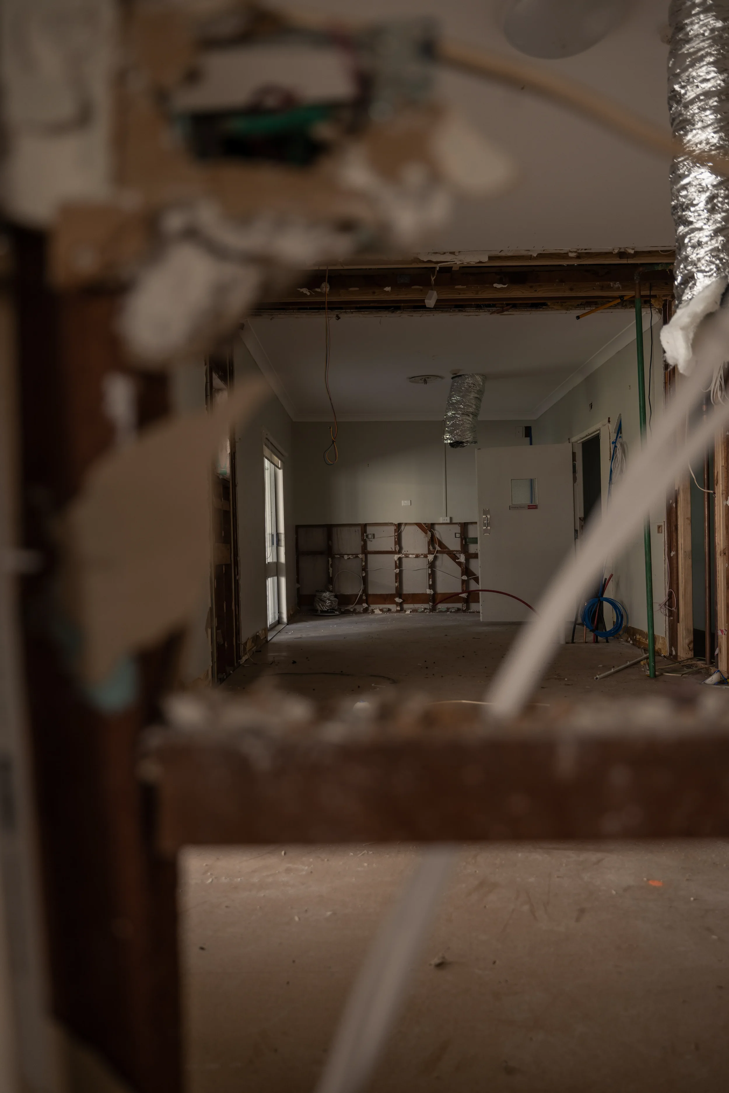 View of an unfinished room under renovation, with exposed pipes and wires, construction materials, and debris on the floor.