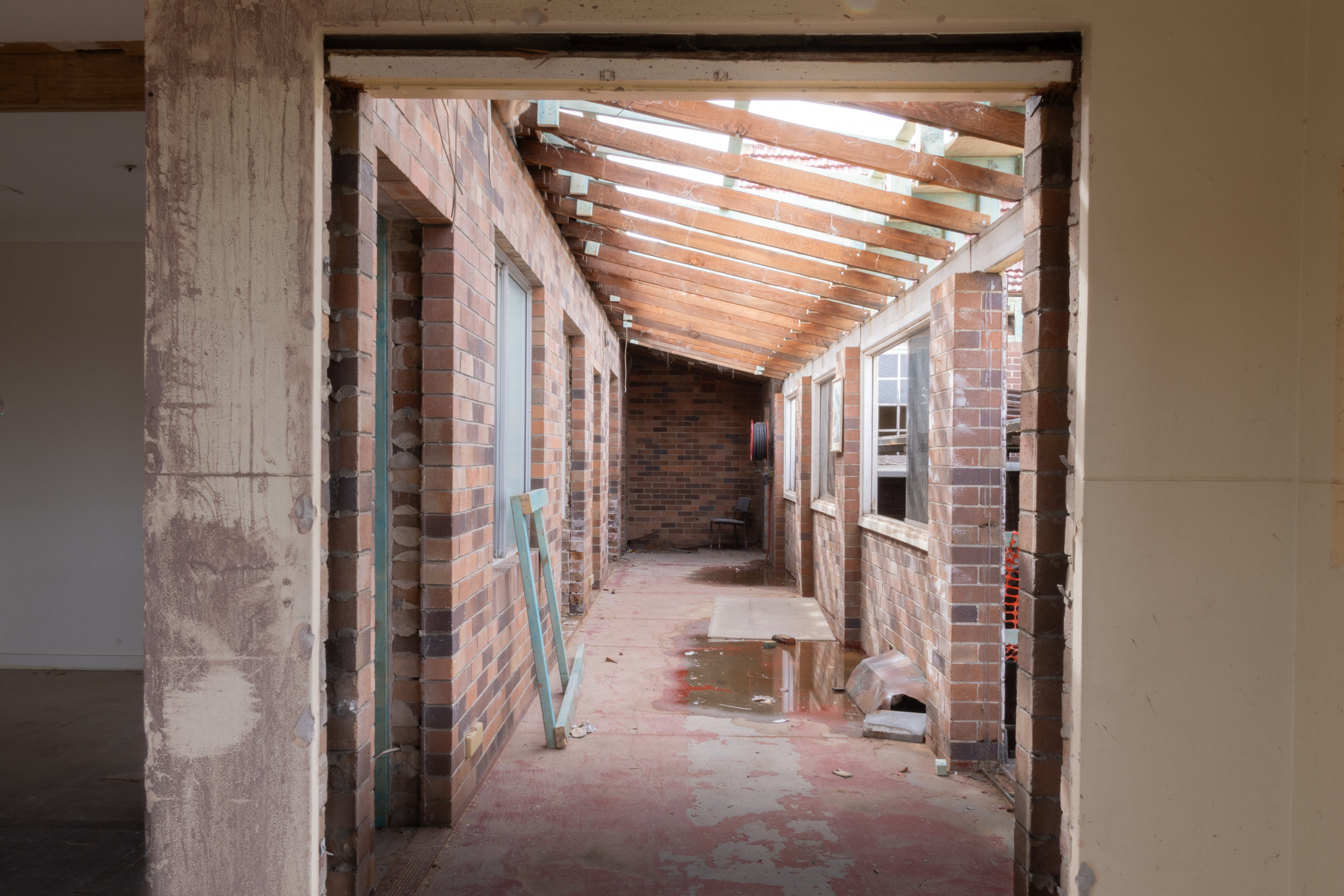 Construction area with unfinished brick walls, wooden roof framework, and open windows, indicating in-progress building renovation or extension.