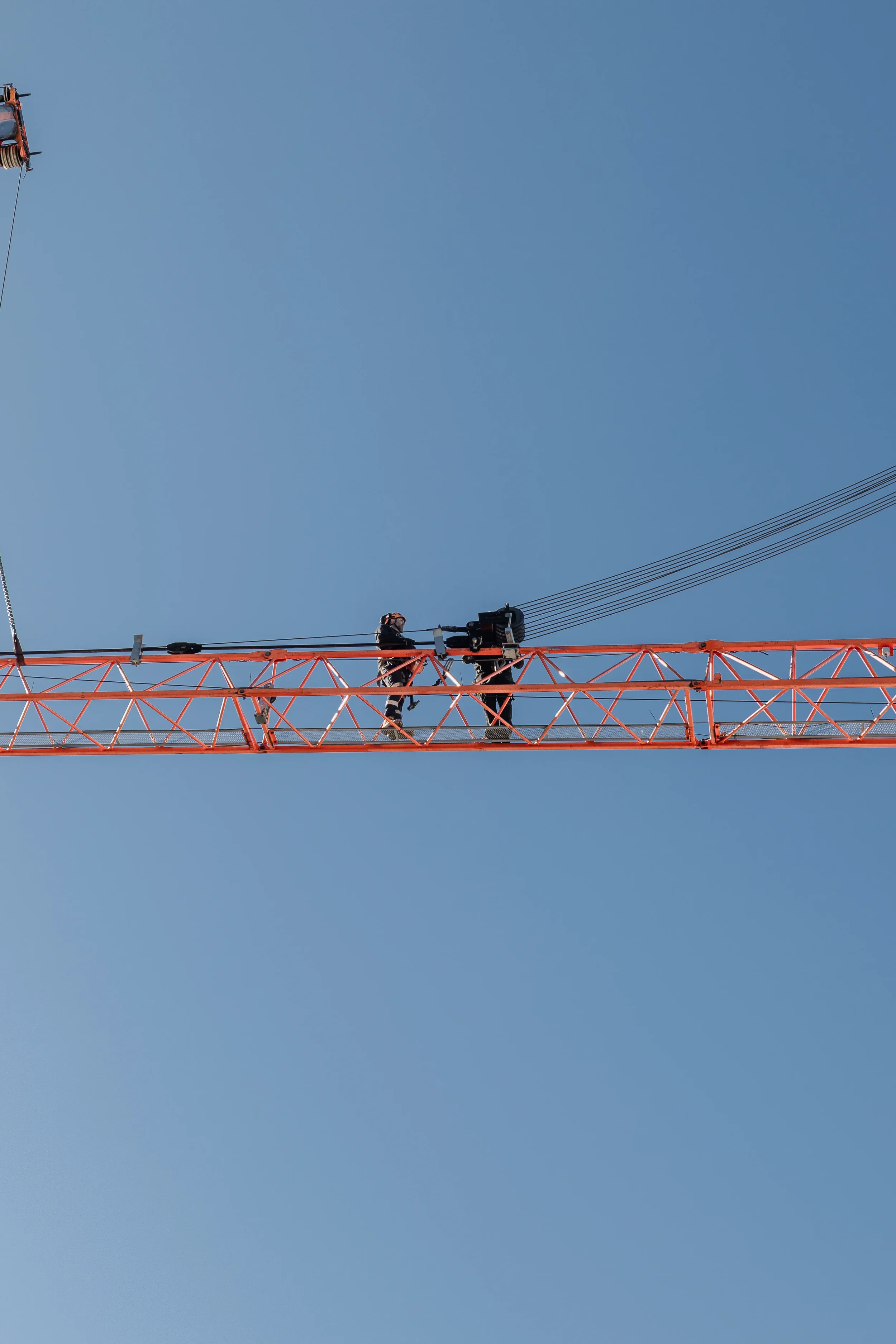 Construction workers on a tall orange crane against a clear blue sky.