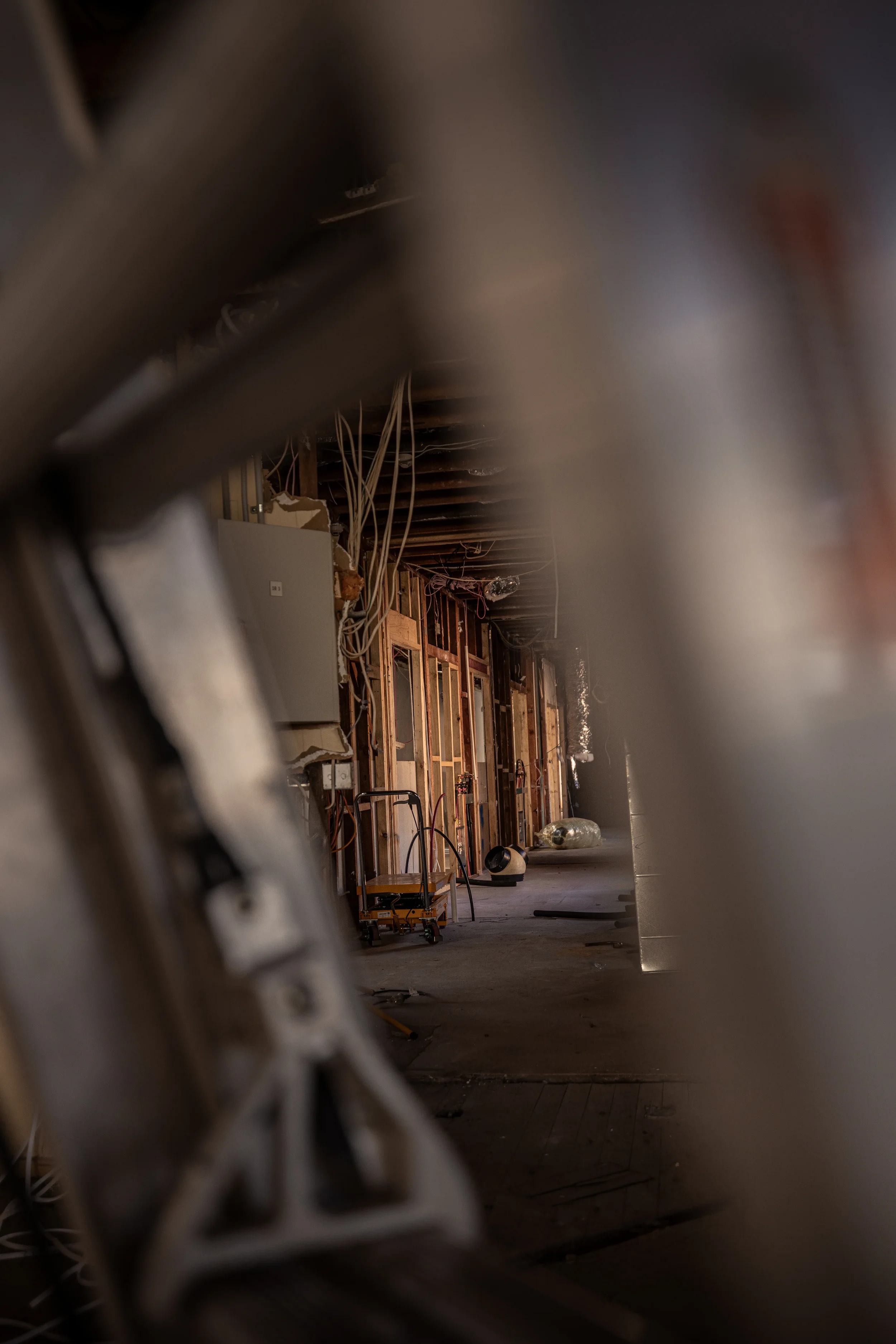 View of a basement or unfinished room with electrical wiring, wooden framing, and construction materials seen through a blurry foreground.