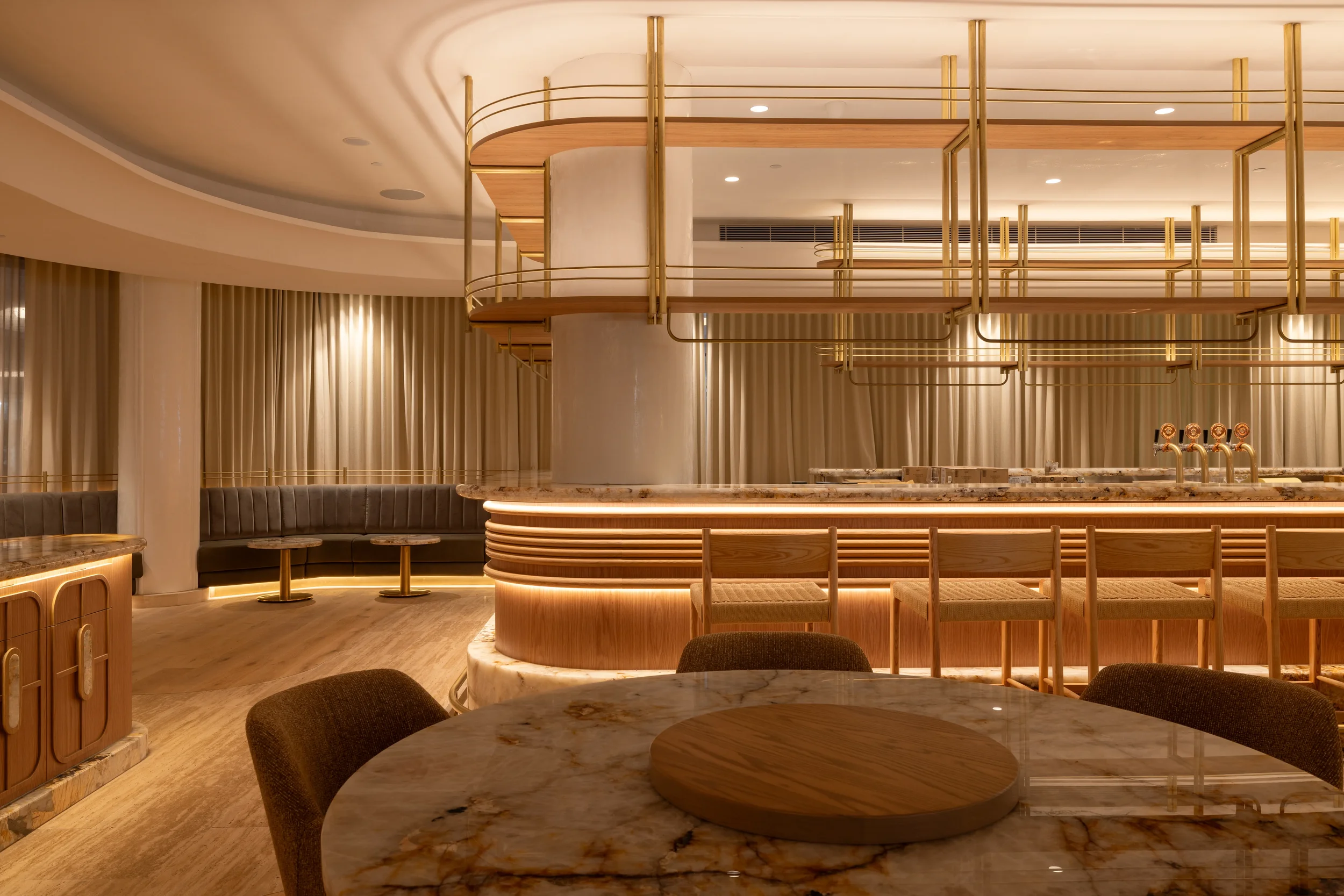 Elegant bar area with a curved marble countertop, seating, and gold accents, illuminated with warm lighting.