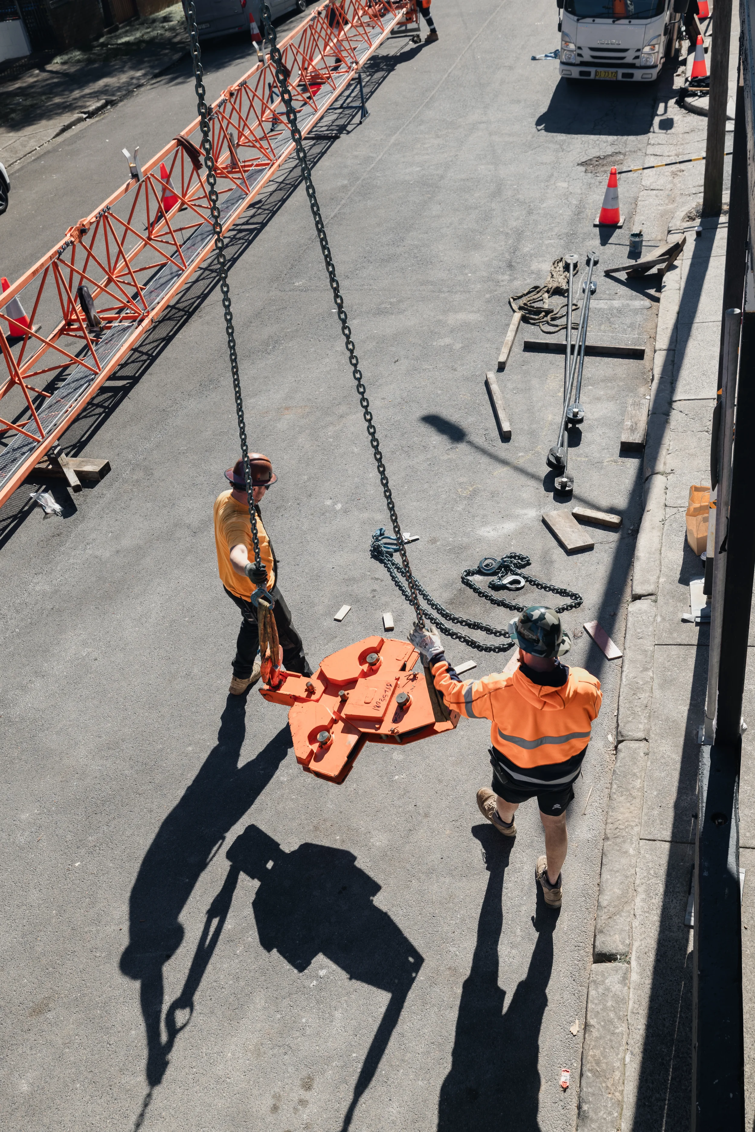 Construction workers installing or repairing a street infrastructure using heavy equipment, with safety cones and tools on the sidewalk.