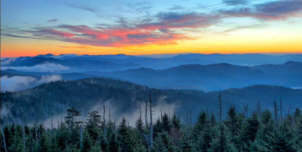 Scenic sunset view over the Smoky Mountains with layered blue ridgelines and forested valleys.