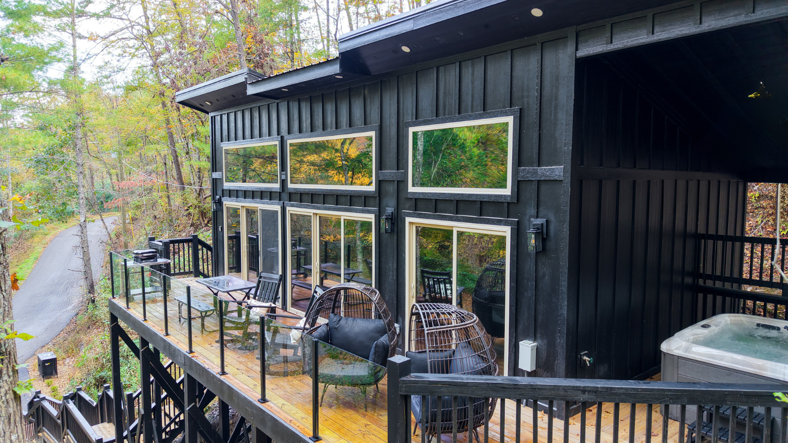 Modern black cabin in Sevier County, Tennessee featuring a balcony, glass railing, and wooded Smoky Mountain surroundings.