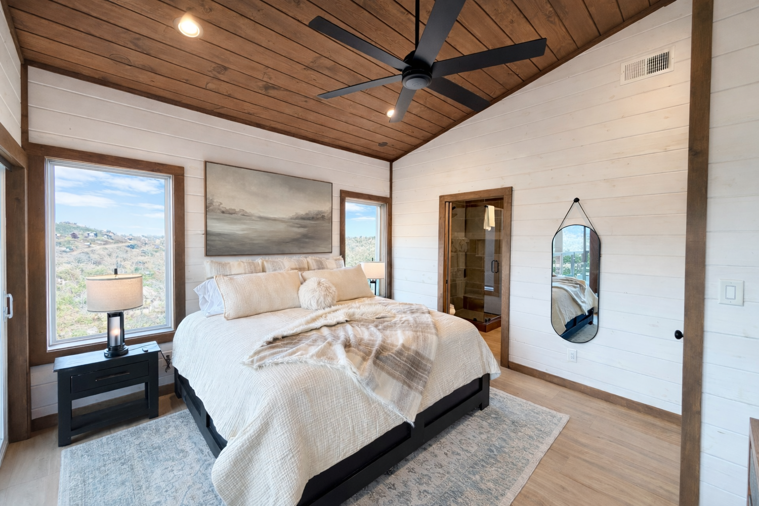 Primary bedroom interior in a Smoky Mountain cabin featuring vaulted wood ceiling, neutral bedding, large windows with mountain views, and modern rustic interior design.