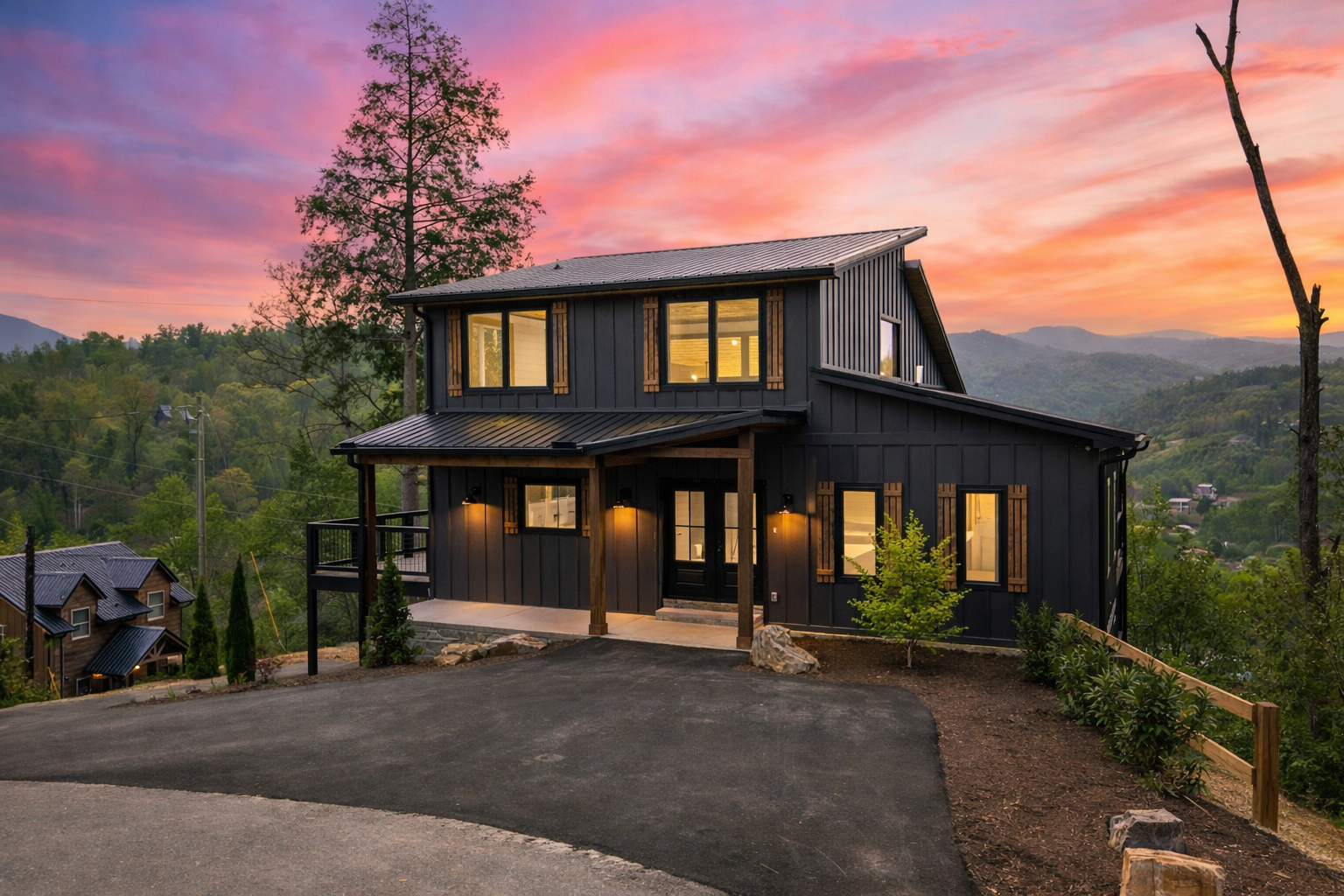 Contemporary mountain cabin in Gatlinburg, TN with black siding, metal roof, and wooded surroundings at dusk.