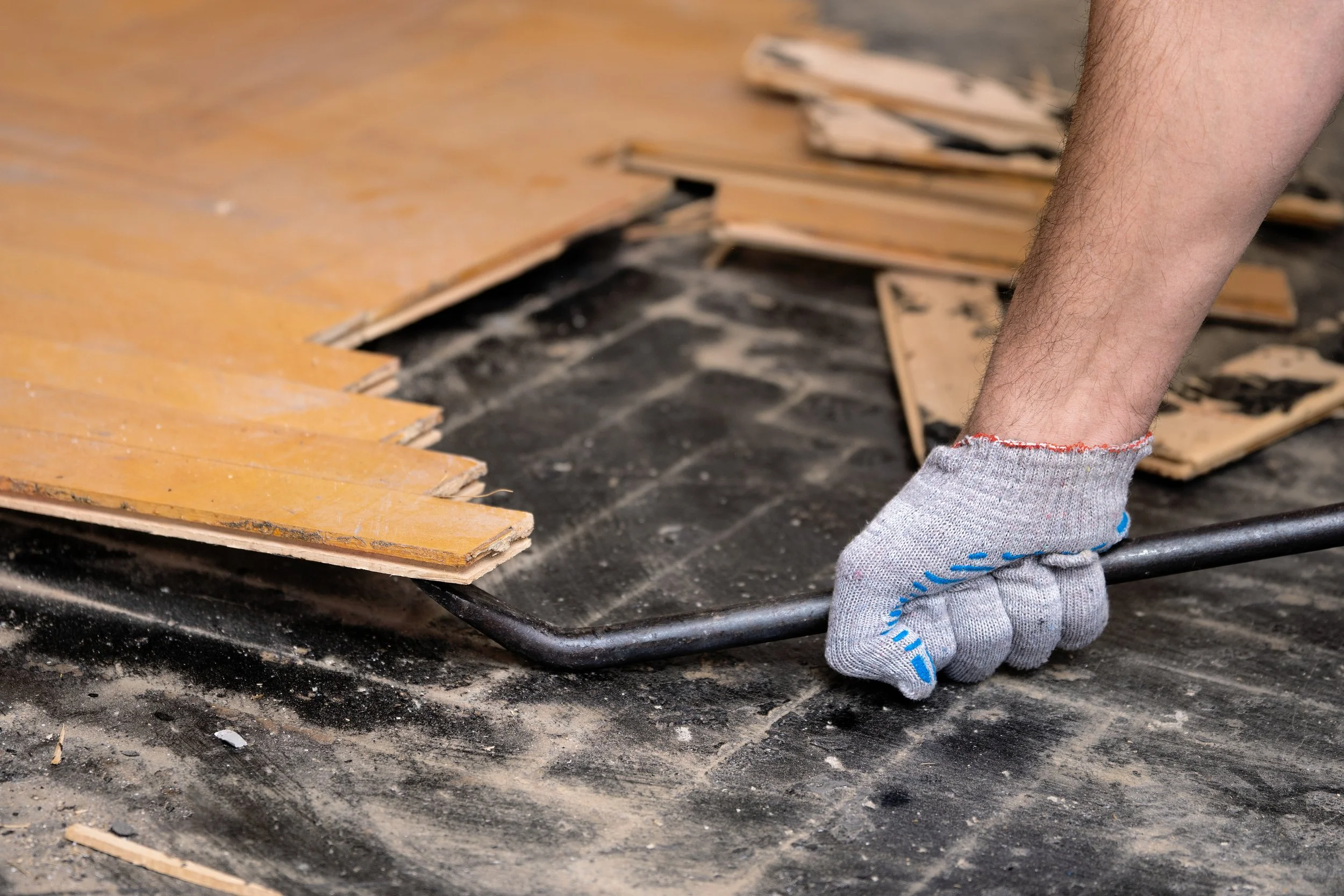 Person wearing gloves is pulling a dragging tool on a dusty, scratched floor, with wood pieces in the background.