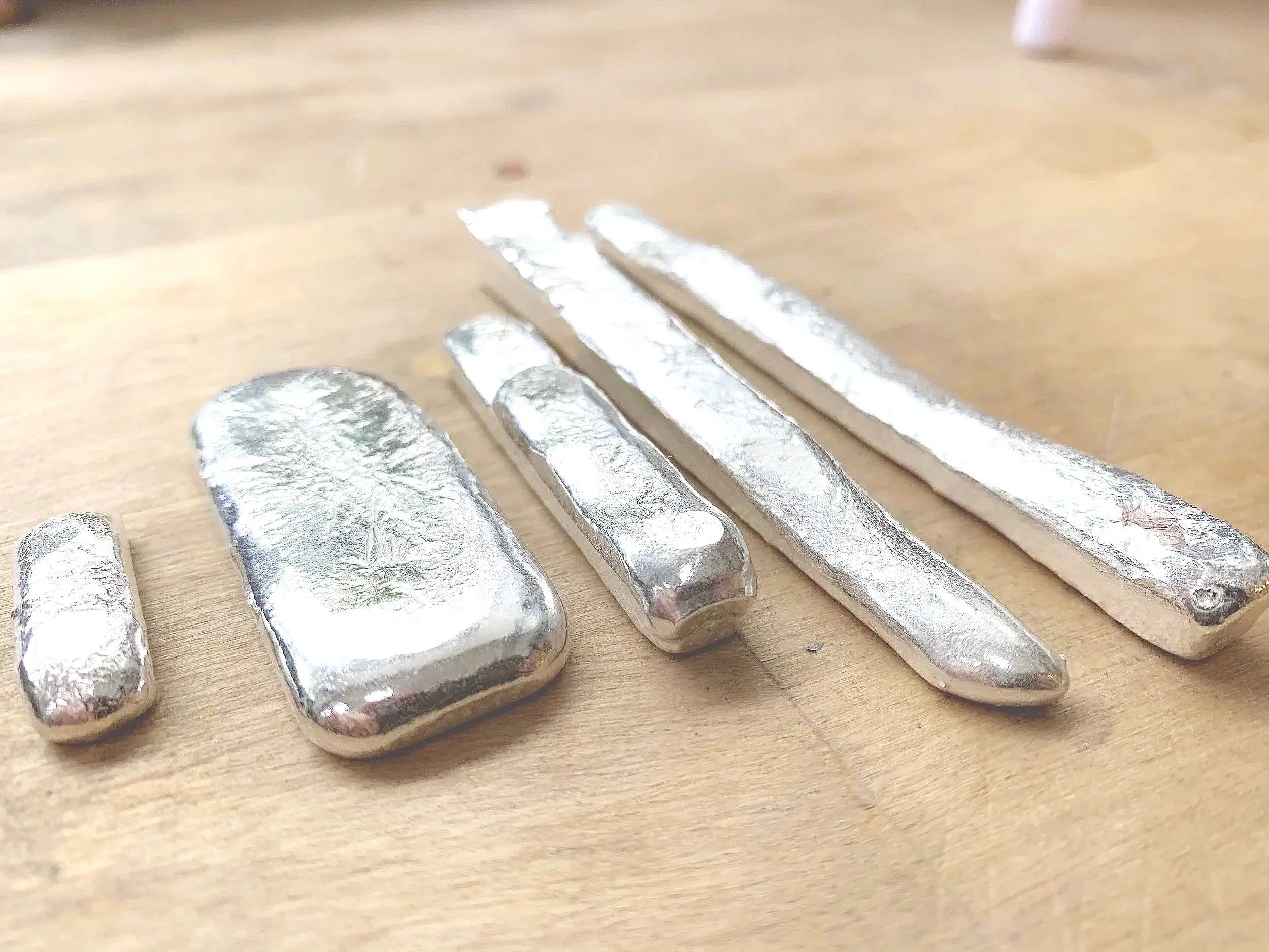 A row of small and large silver-colored metal bars laid out on a wooden surface.