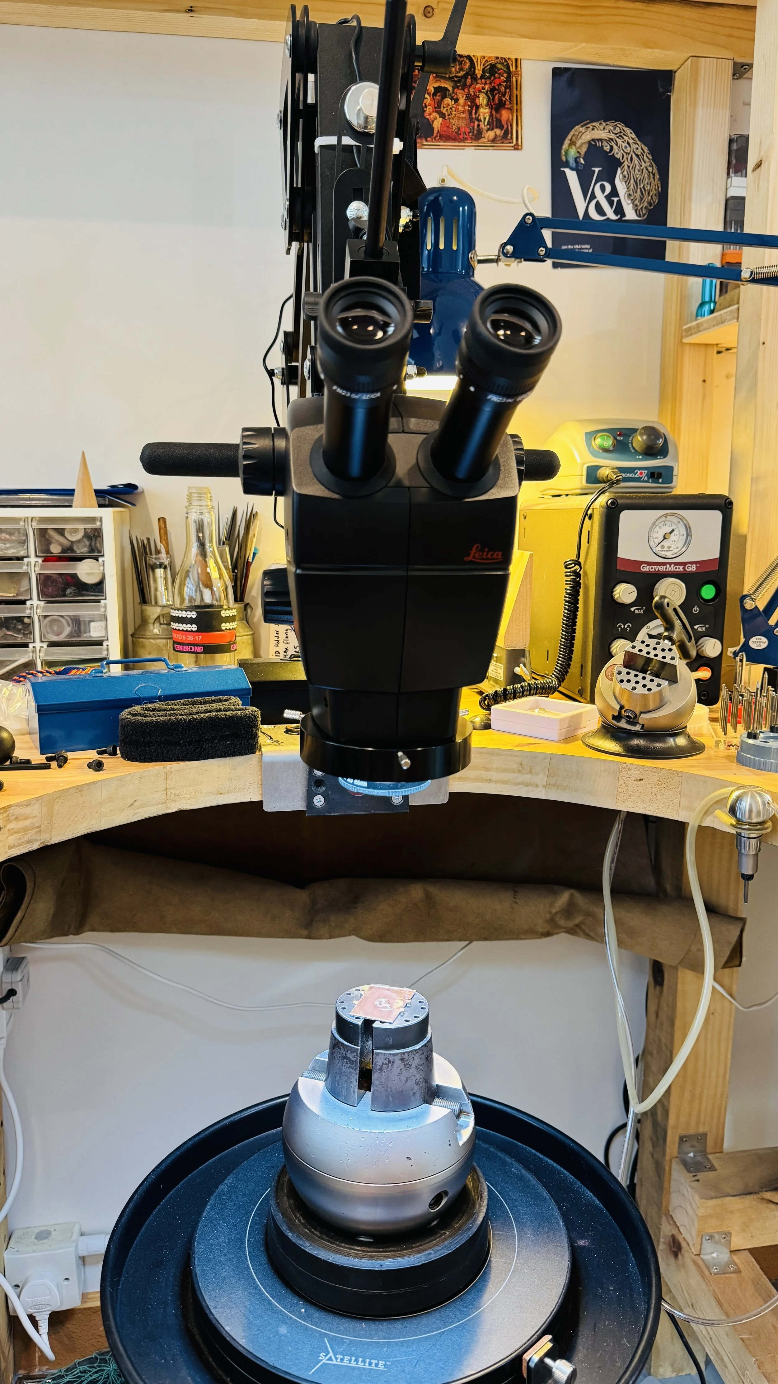 A microscope set up on a workbench in a workshop, with various tools, equipment, and art on the wall in the background.