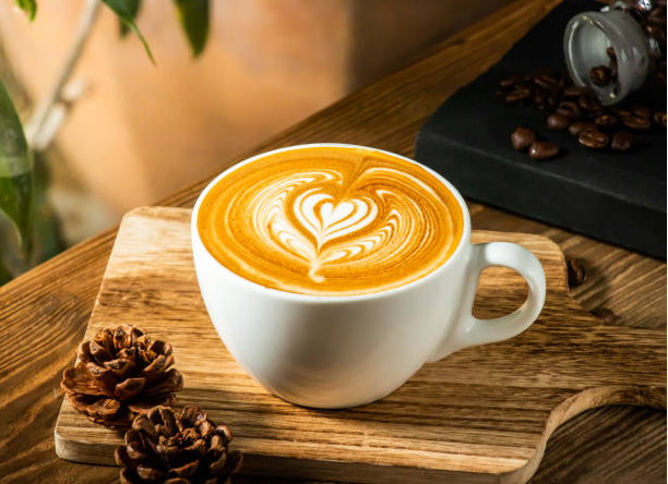 A cup of latte with heart-shaped latte art on top, placed on a wooden tray with pinecones, on a wooden table.