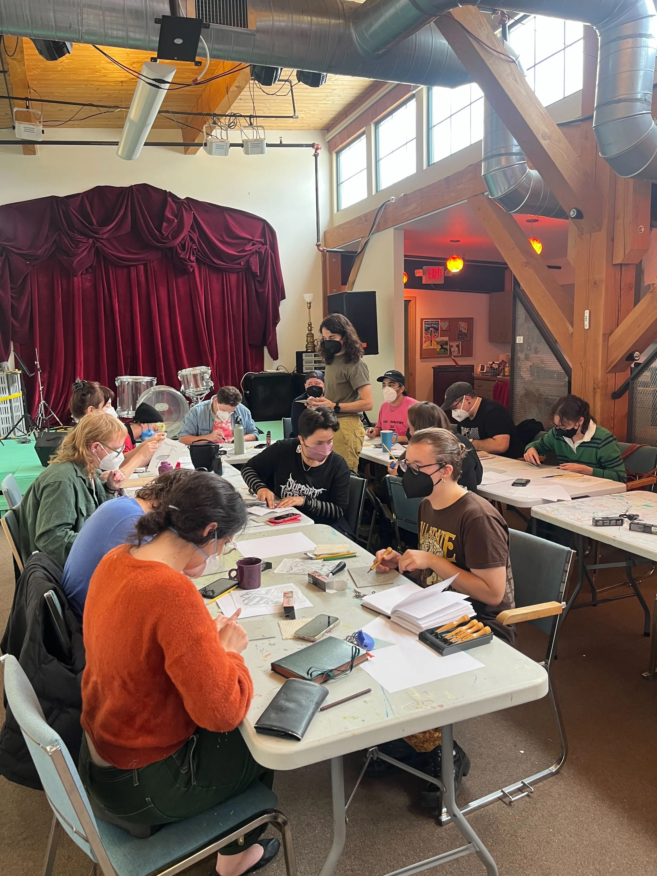 group of people in masks sitting at tables creating art at communication madison