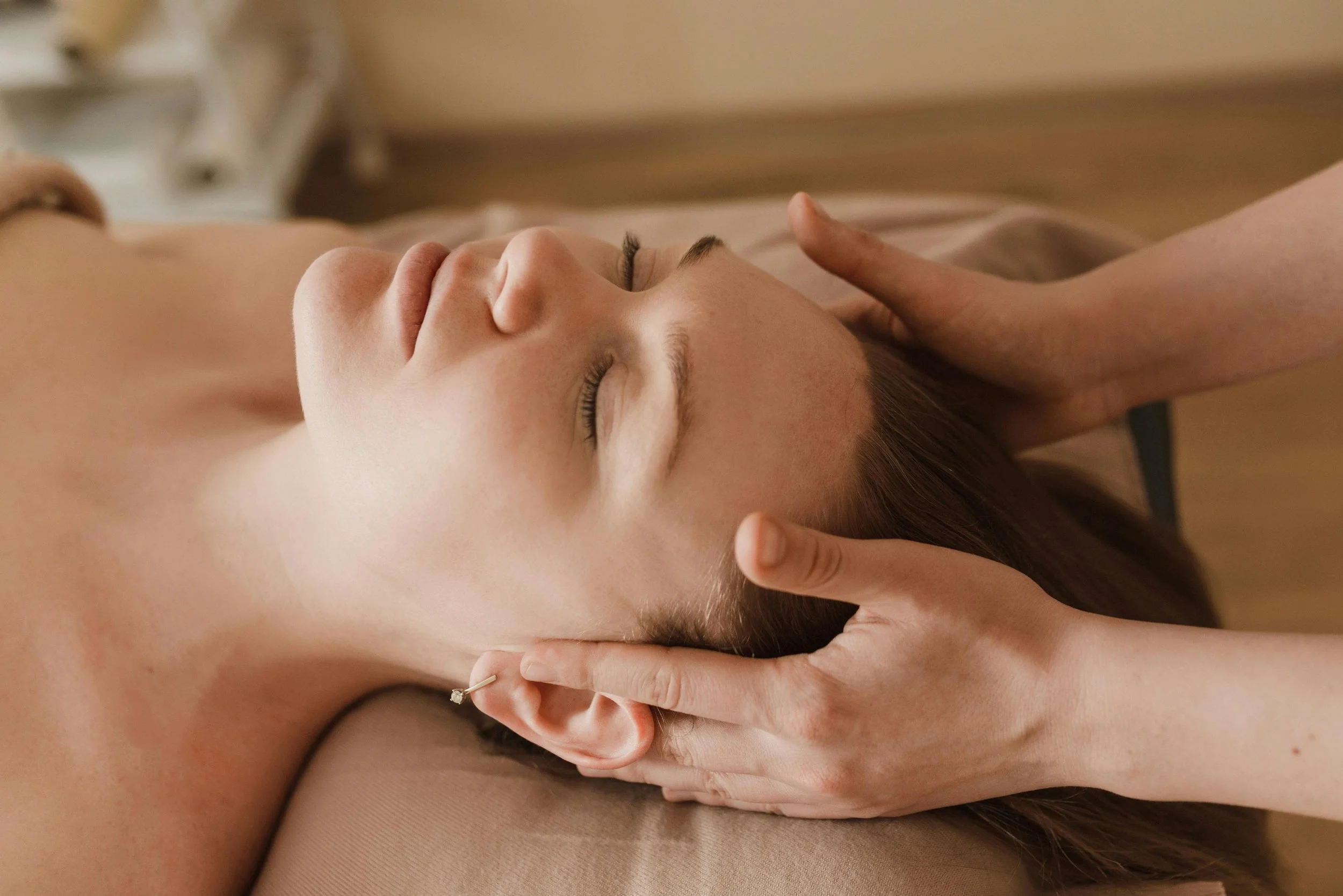 A woman receiving a massage therapy session, lying on her back with eyes closed, while a therapist gently holds her head in milton, delaware at a spa..