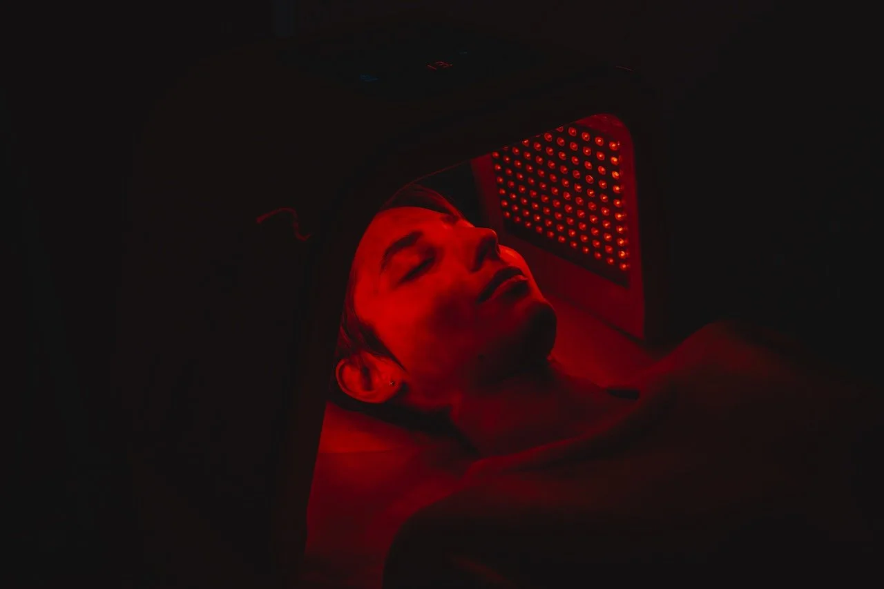 A person receiving red light therapy on their face in a dark room.