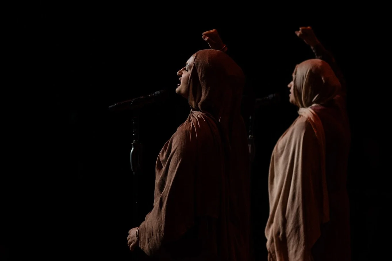 Two women wearing brown headscarves and long brown robes performing poetry slam.