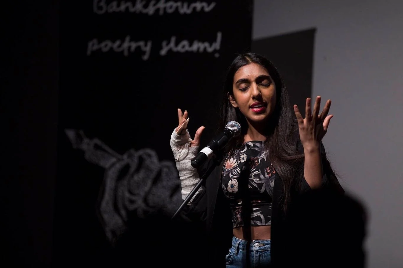 A young woman with long dark hair performing poetry on stage.