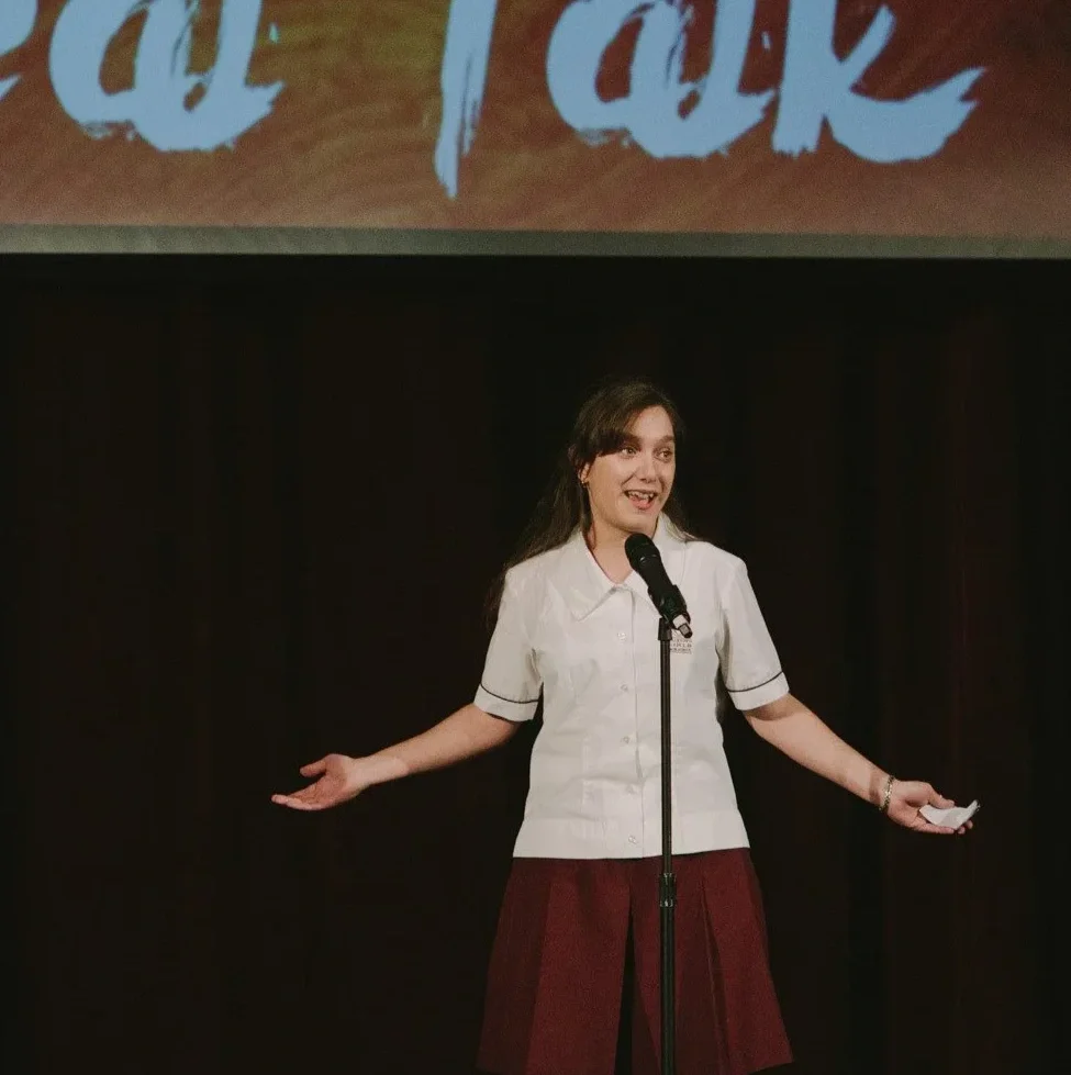 A young girl in a school uniform performing at a realtalk poetry slam.