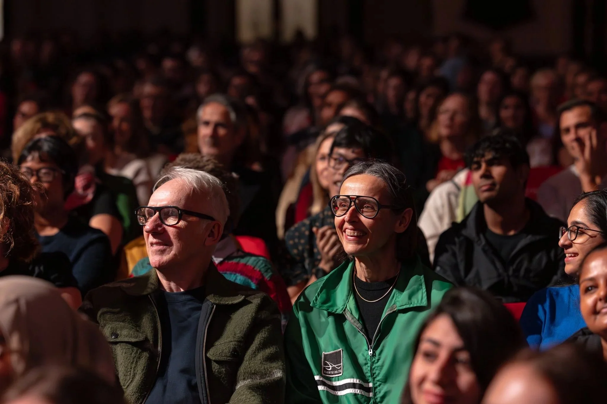 An audience of diverse men and women seated in a dark theater.