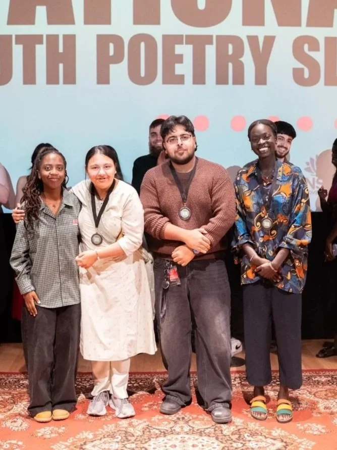 Group of five diverse people standing on a stage with medals around their necks, smiling, at a poetry competition or event.
