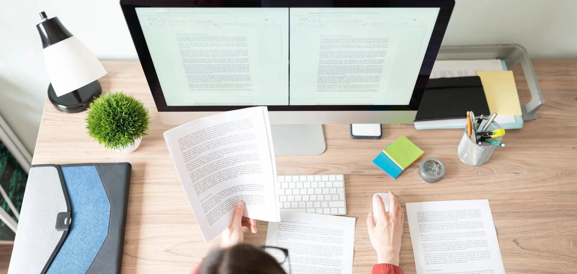 Copyeditor at desk reviewing a digital and paper manuscript.