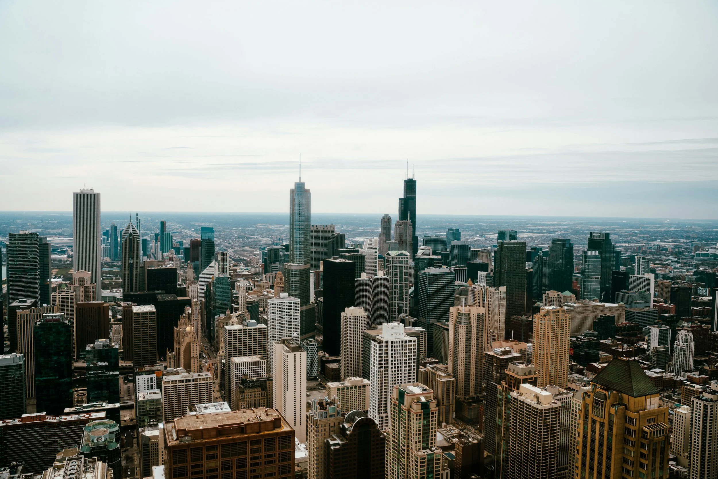 A high-angle view of a dense downtown skyscraper cityscape with various tall buildings and overcast sky.