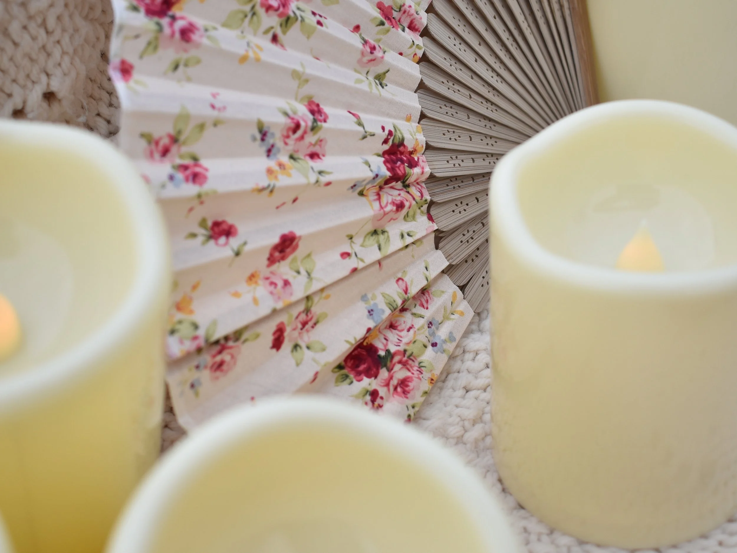 Close-up view of a floral fabric and a stack of paper or books, with two yellow candles in the foreground.