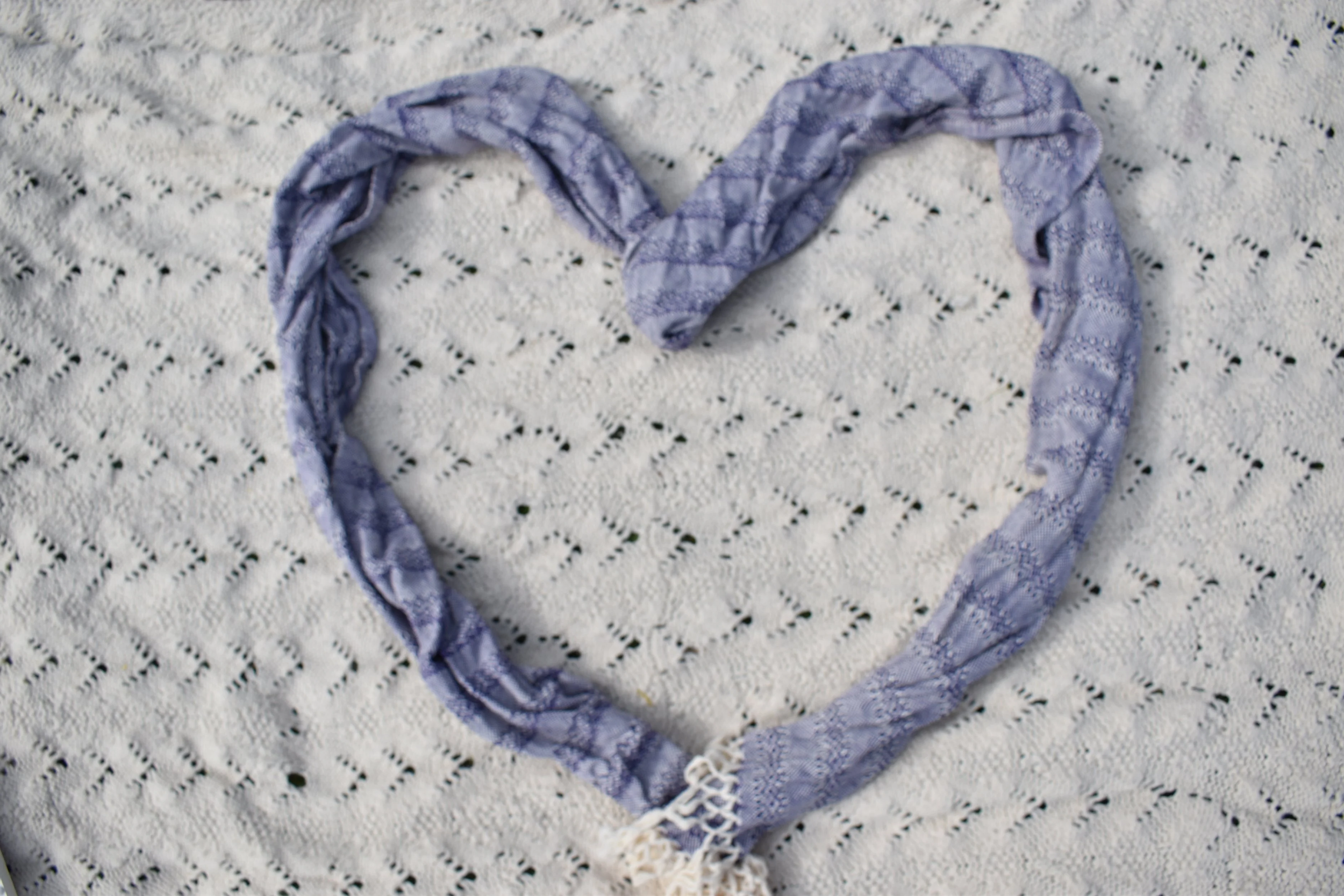 A purple lace scarf arranged in a heart shape on a white lace tablecloth.