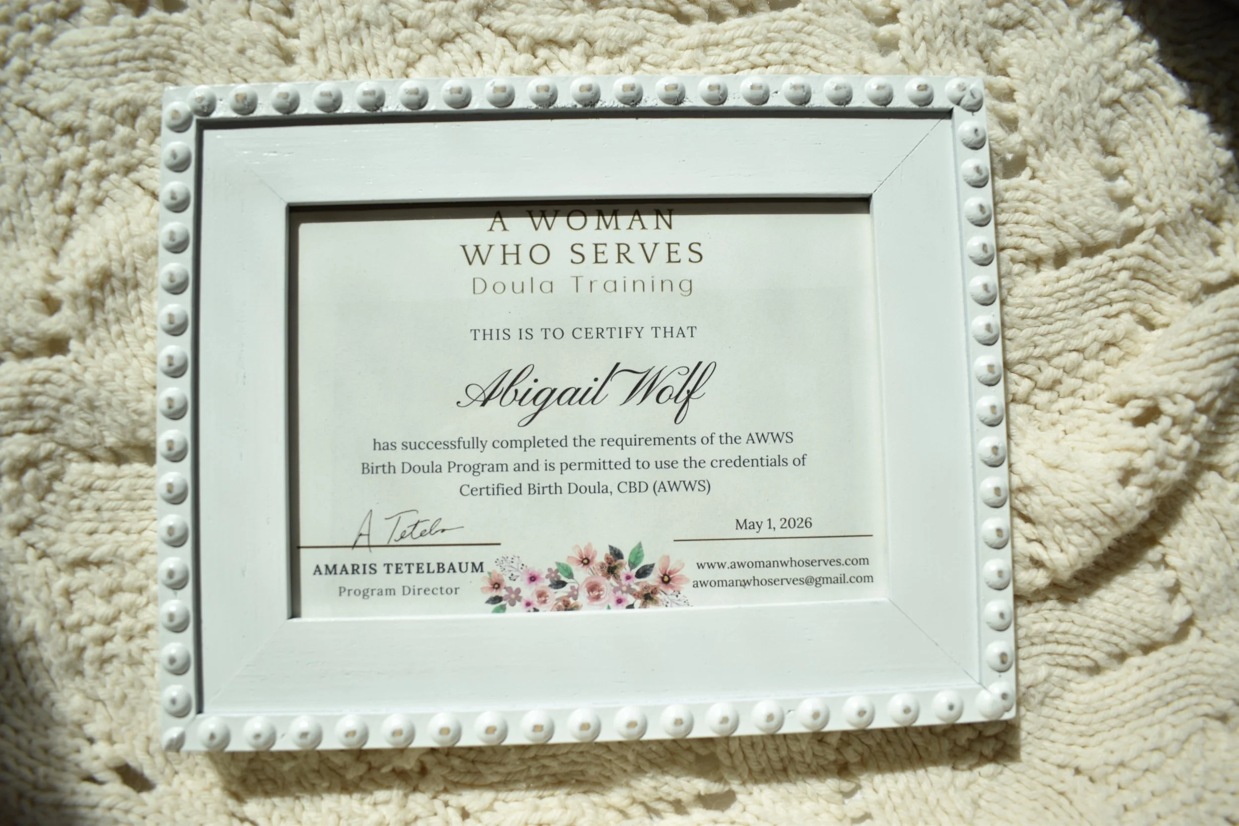 Certificate awarded for doula training, signed by Amaris Tetelbaum, with floral decoration at the bottom, placed on a textured cream-colored blanket.