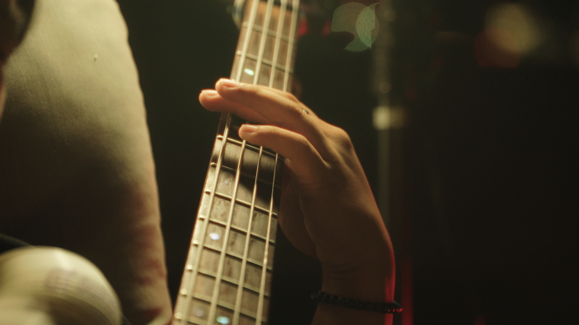 Close-up of a person's hand playing an electric guitar, with a dark background and bokeh lights.