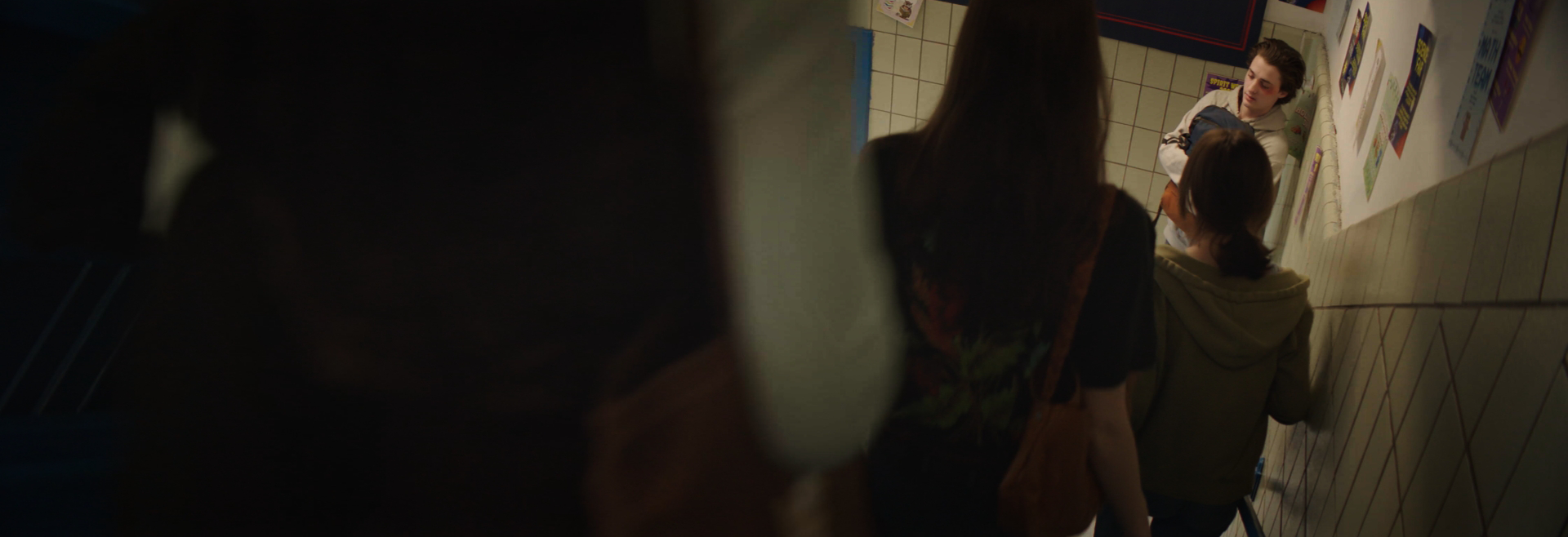 Three students walking up a school staircase while talking, with posters on the wall beside them.