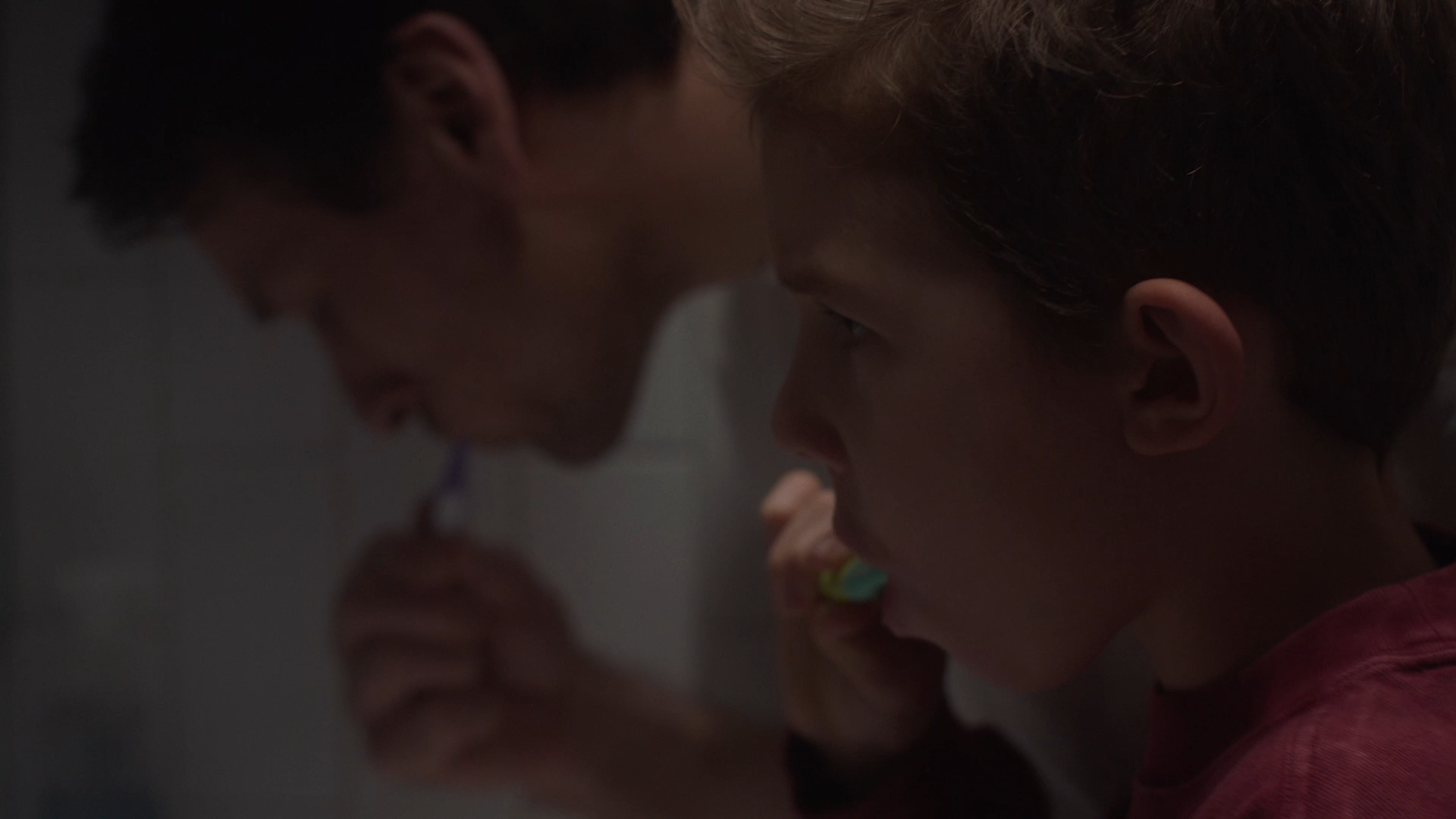 Father and son brushing their teeth in the bathroom, close-up.