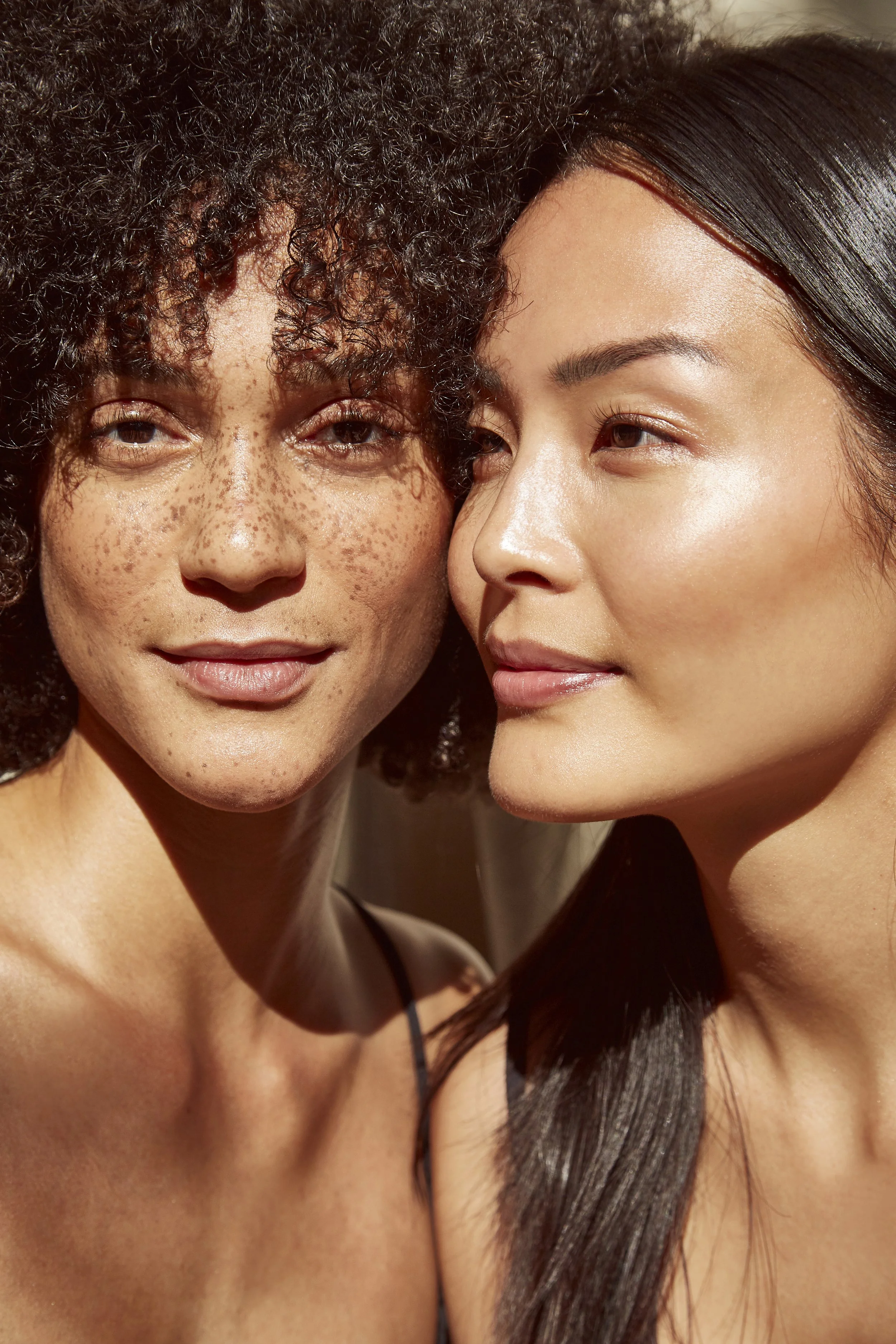 Close-up of two women, one with curly hair and freckles, and the other with straight dark hair, smiling softly.