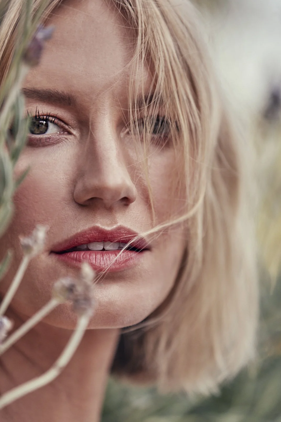 Close-up of a woman's face with blonde hair, partially obscured by lavender flowers.