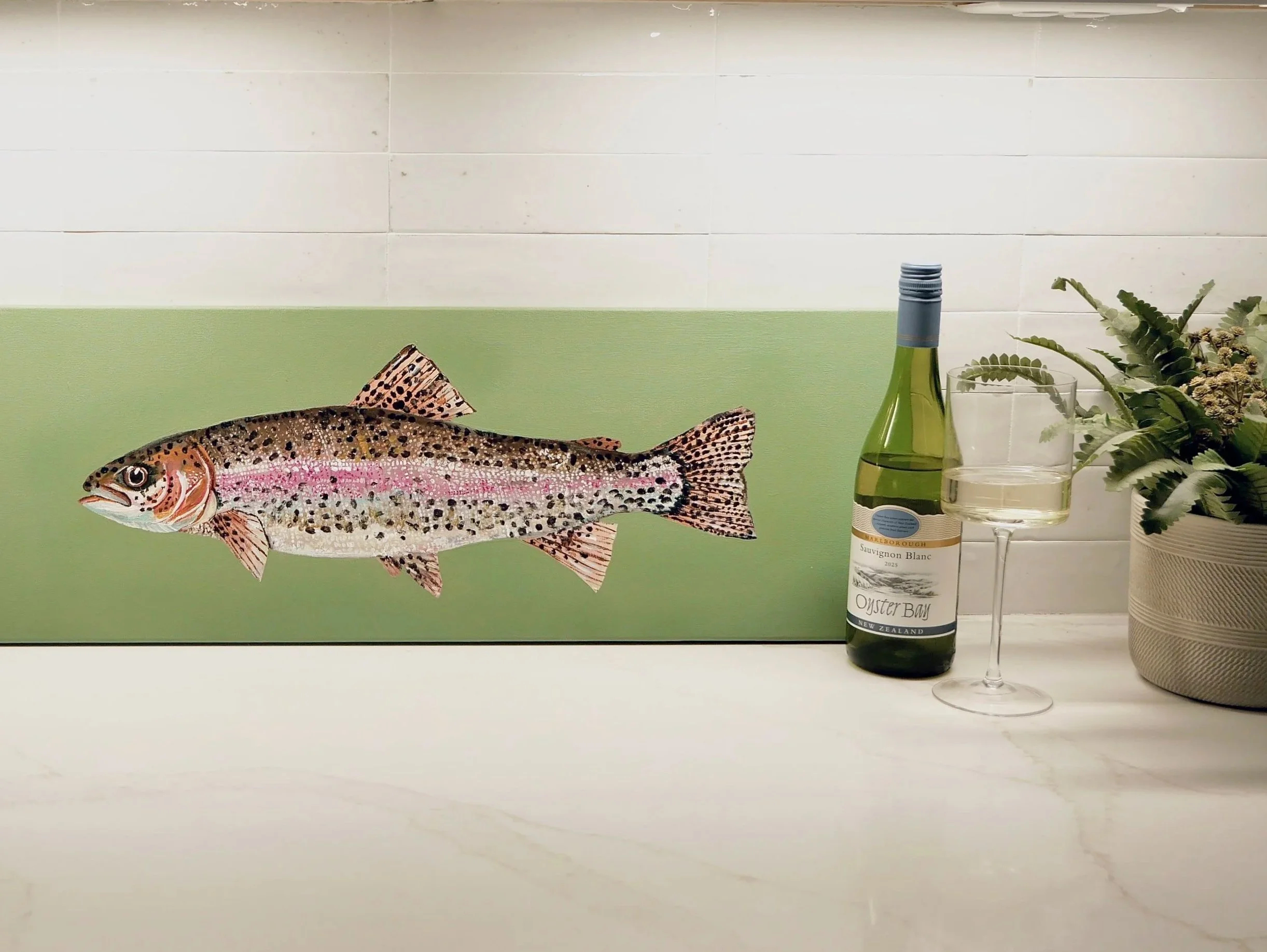 Decorative wall with illustration of a fish, a bottle of Sauvignon Blanc wine, a wine glass with white wine, and a potted plant