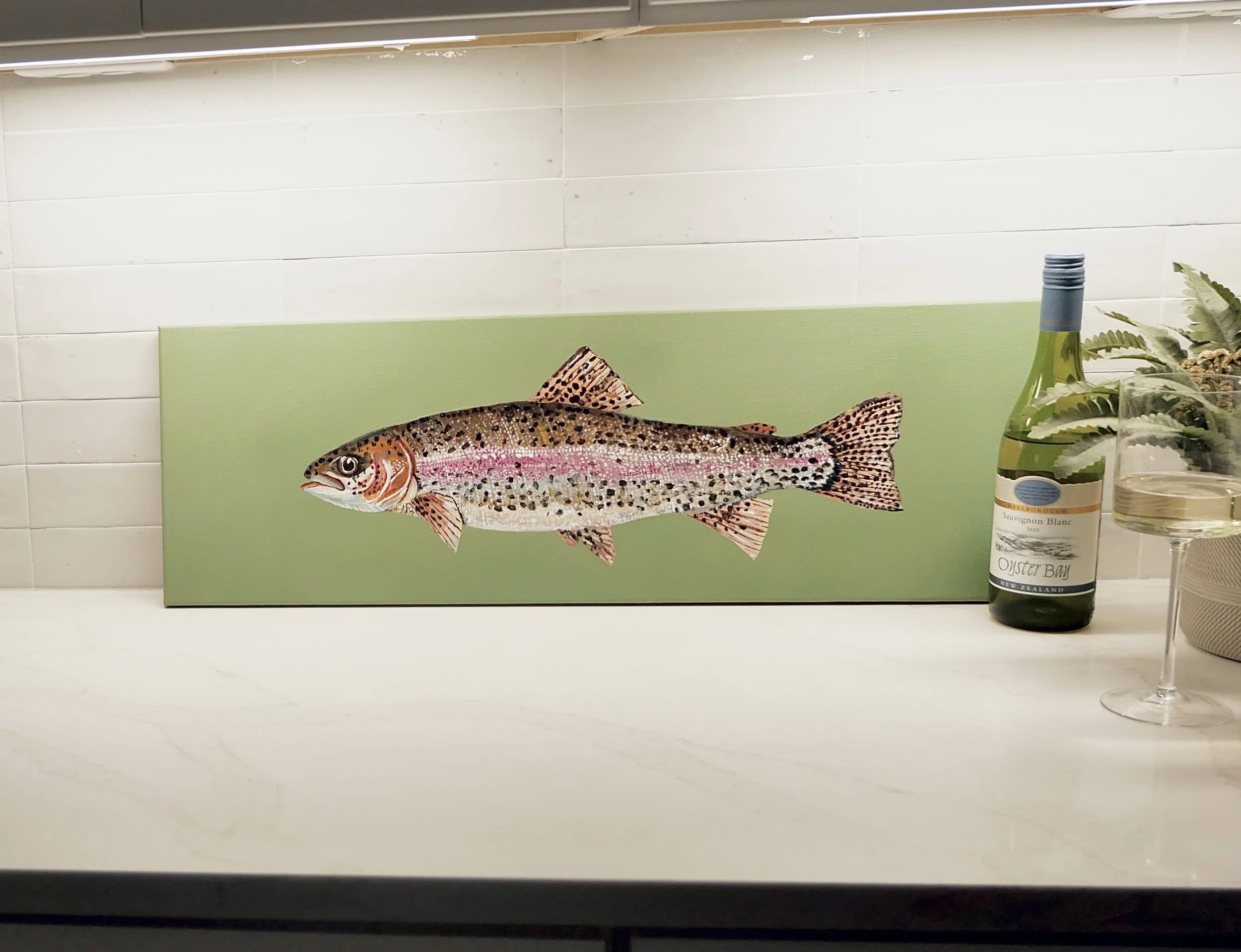 Decorative fish illustration on a green background, placed on a white surface. To the right, there is a bottle of Sauvignon Blanc wine, a glass with white wine, and some greenery.