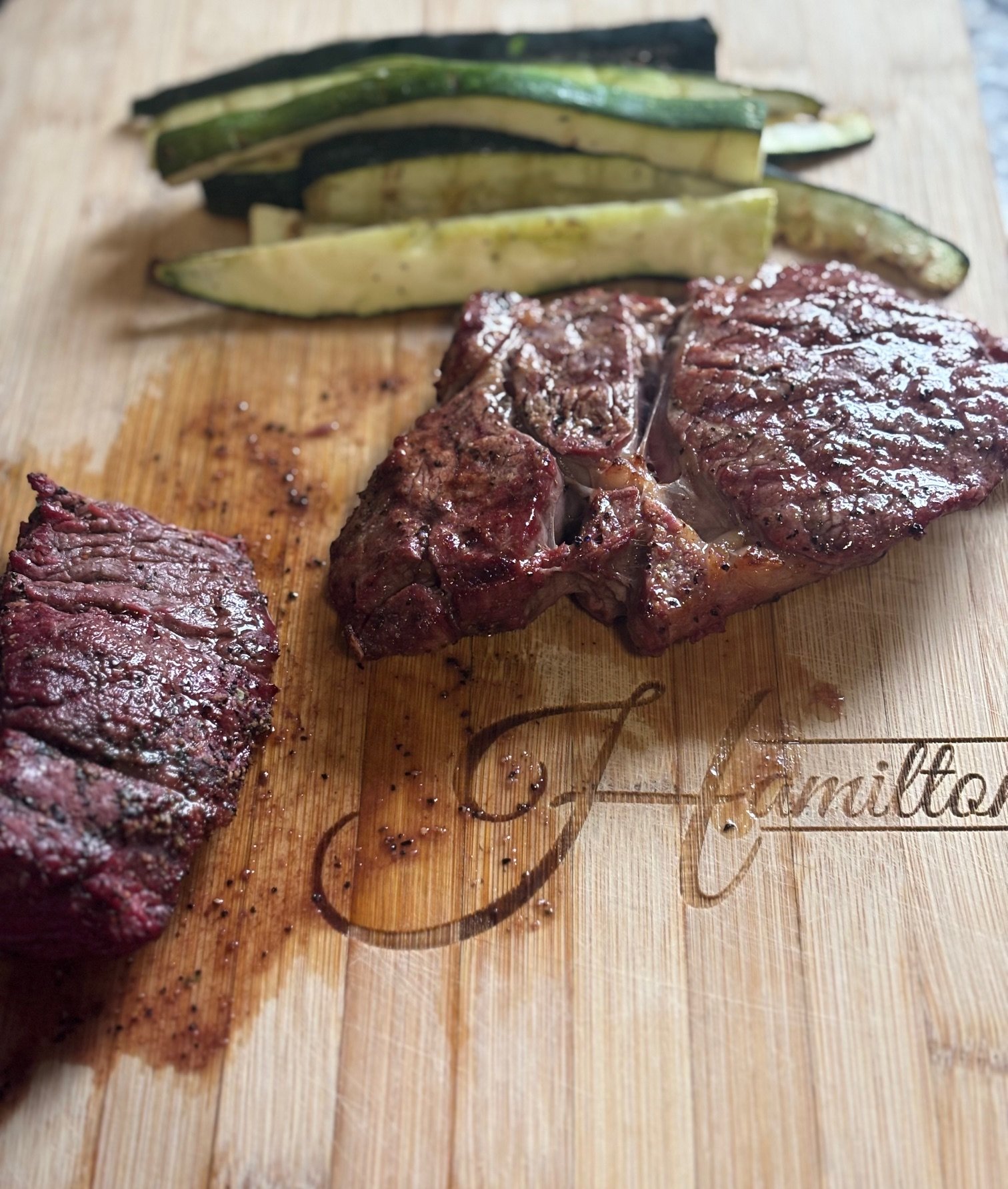 Grilled steak with sliced zucchini on a wooden cutting board engraved with 'family'